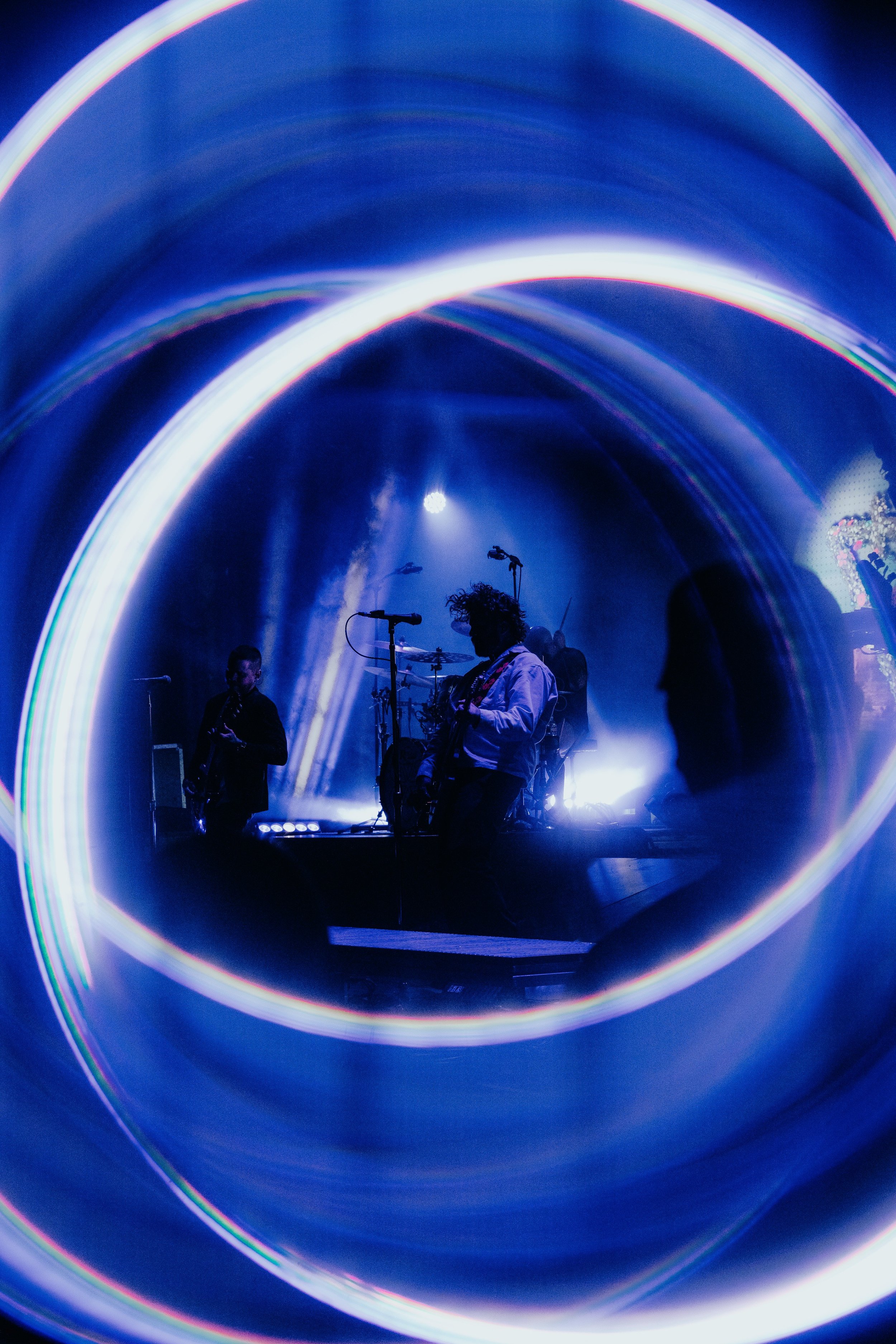 A live music performance inside a tunnel-like space with swirling blue lights and several musicians, including a guitarist and a drummer.