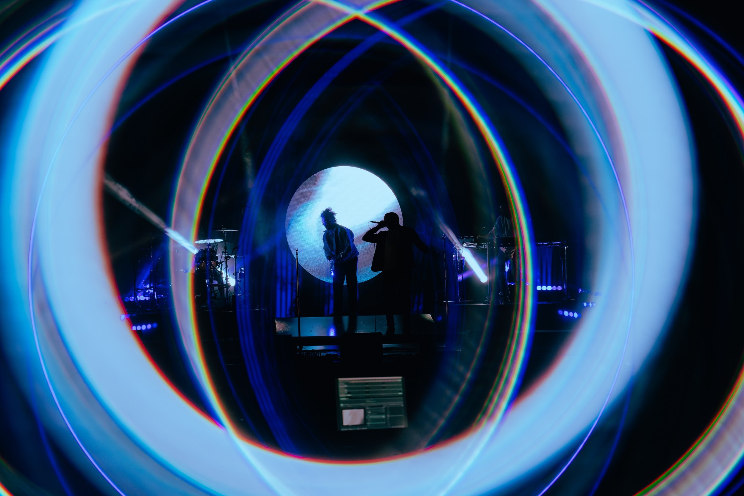 Silhouettes of musicians performing on stage with vibrant, colorful lights creating a tunnel effect around them.