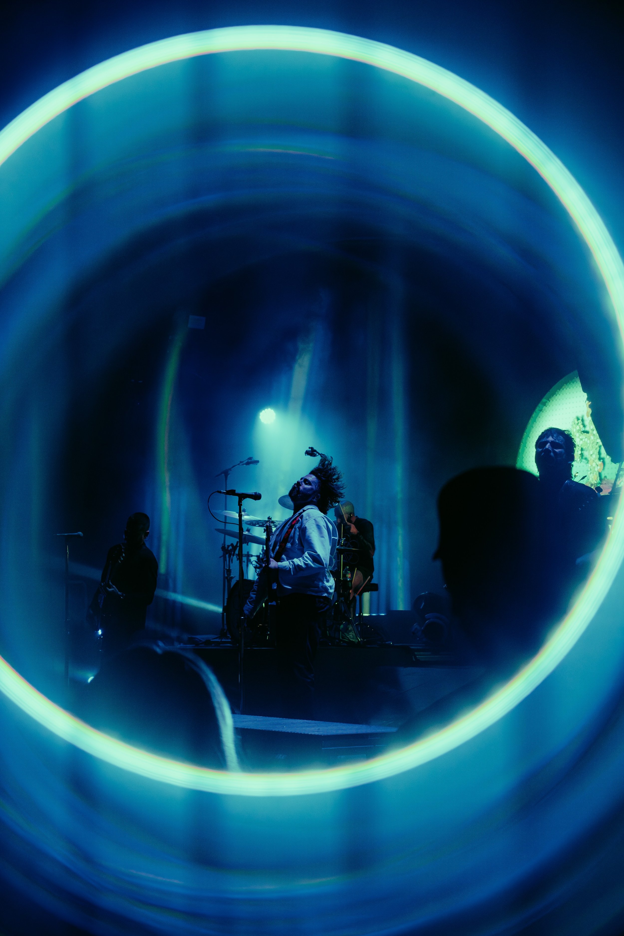 A live music performance with musicians on stage, illuminated by vibrant blue and yellow lighting, viewed through a circular frame.