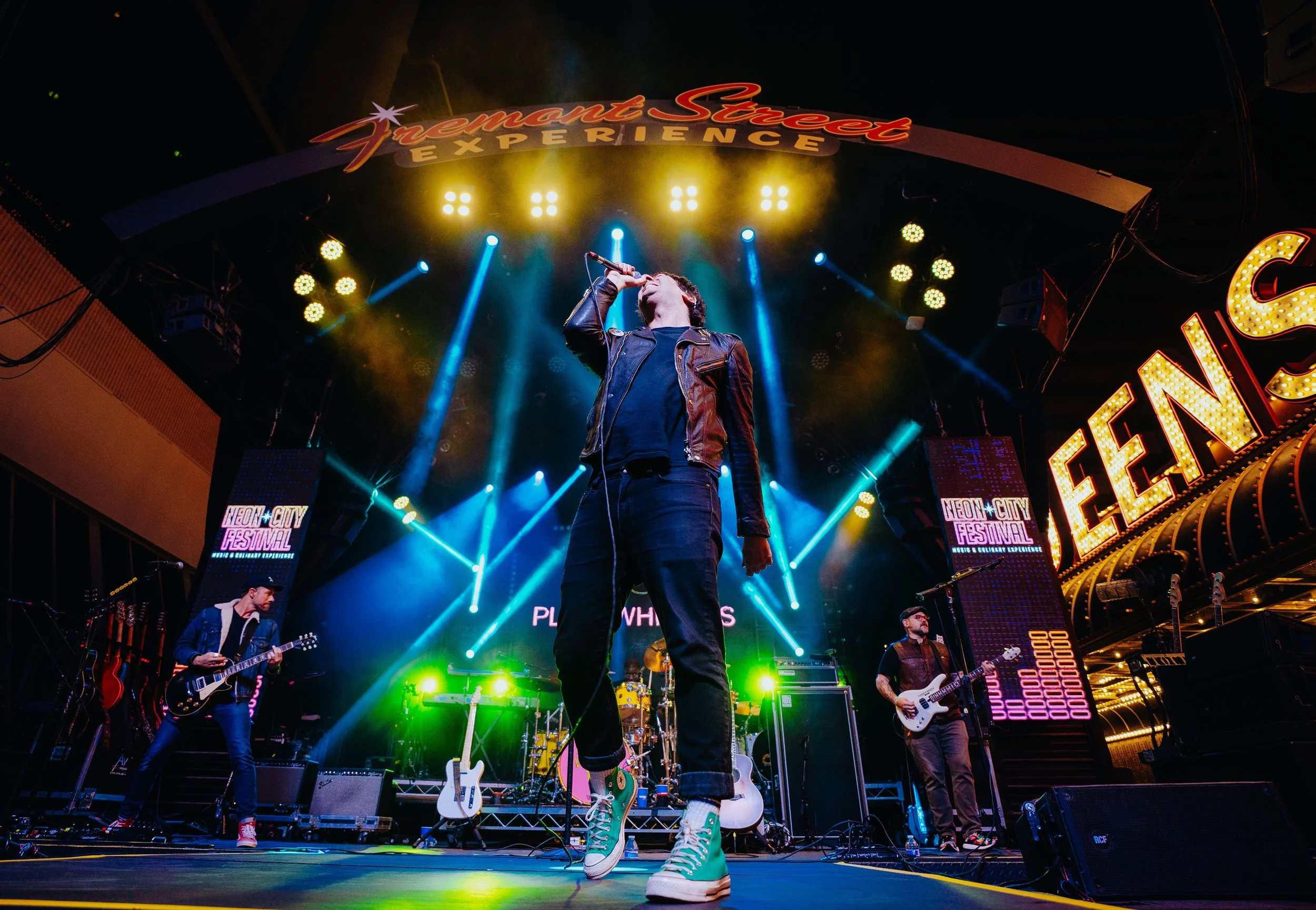Musician performing on stage at the Neon City Festival, with colorful stage lights and a singer in a leather jacket and sneakers at the center.