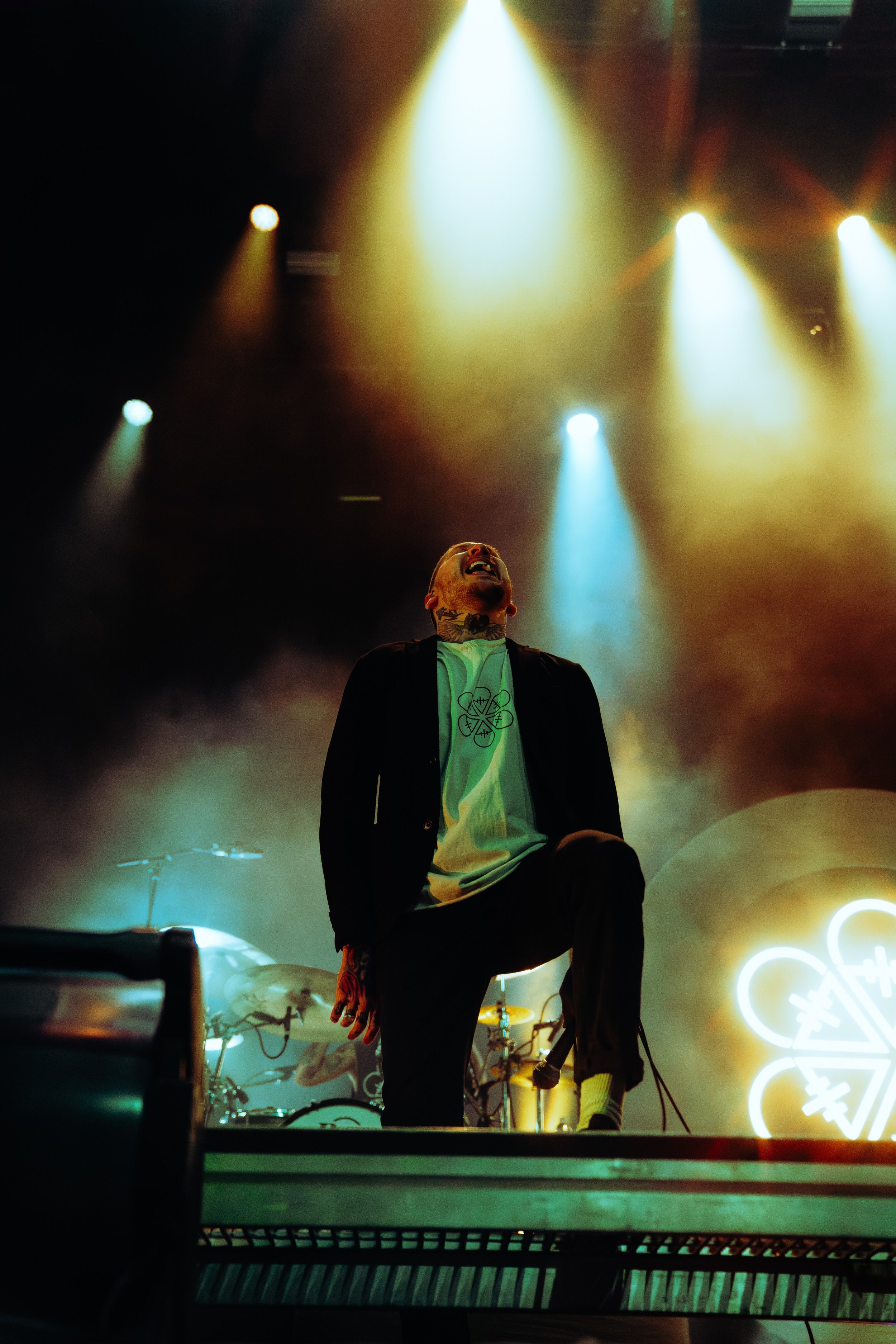 A performer on stage under colorful yellow, blue, and warm stage lights, with a microphone in hand, during a concert.