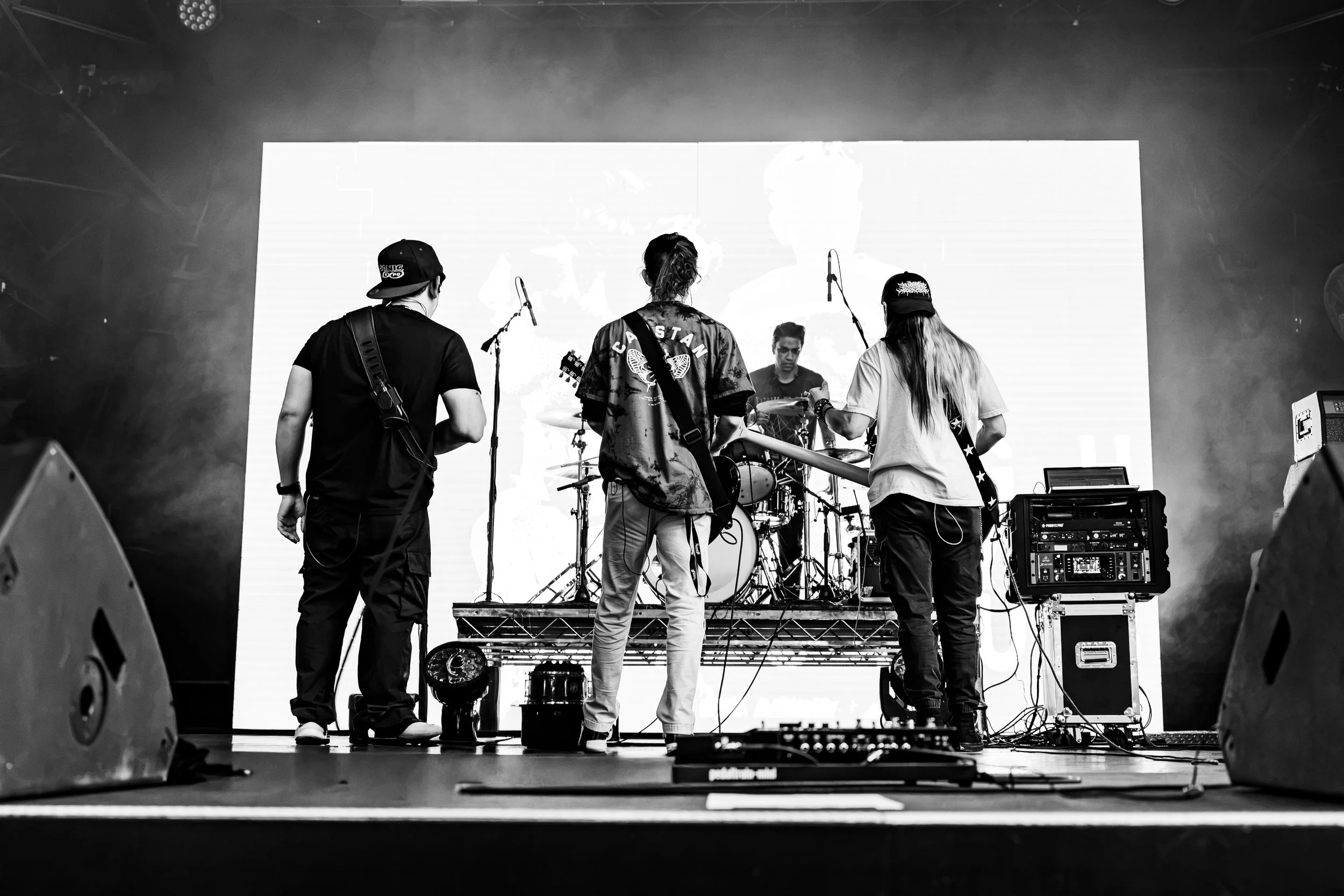 Black and white photo of four people on a stage, preparing to perform, with musical instruments and equipment around them.