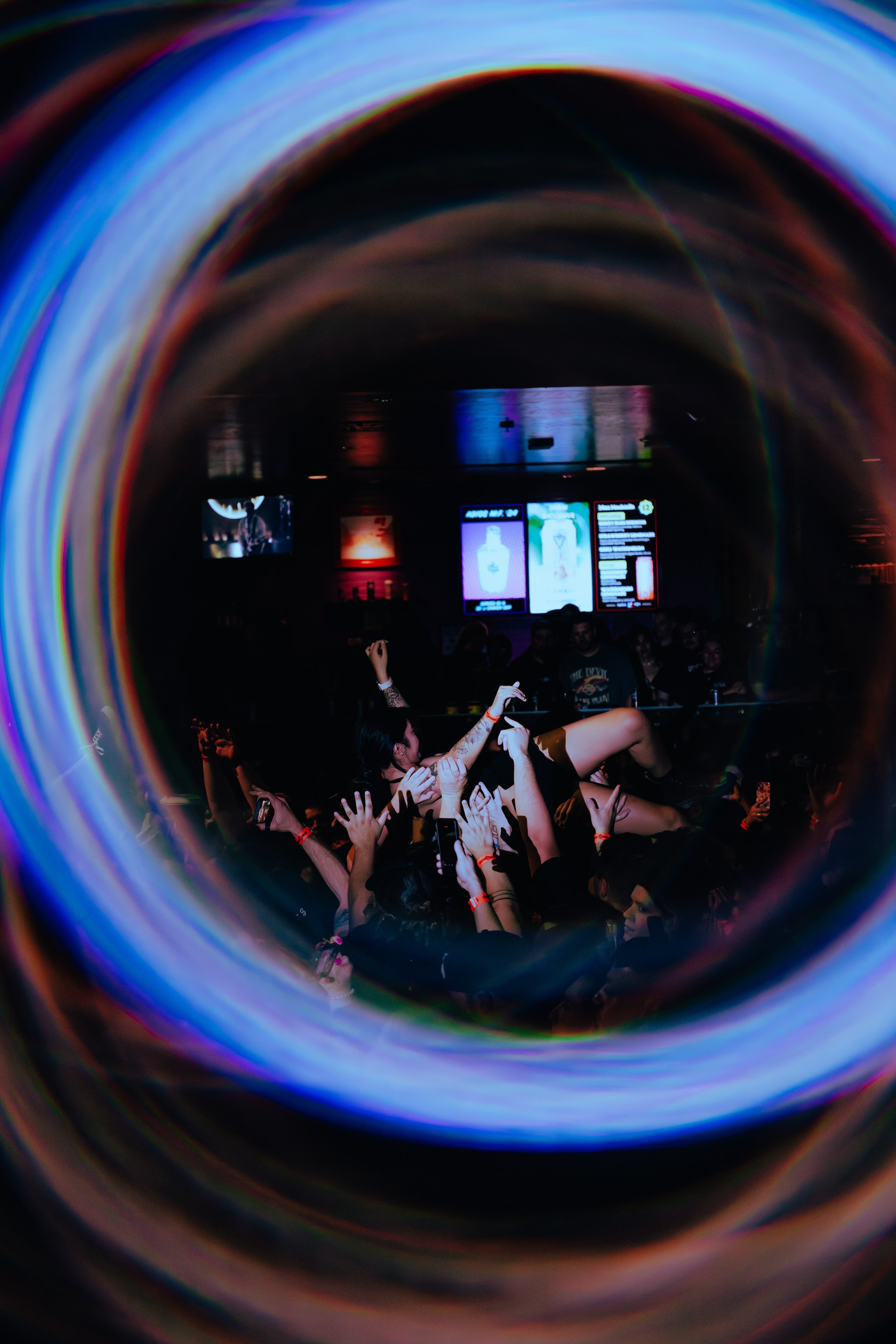 Individuals at a concert or festival with their hands raised, seen through a colorful, swirling image or tunnel effect.