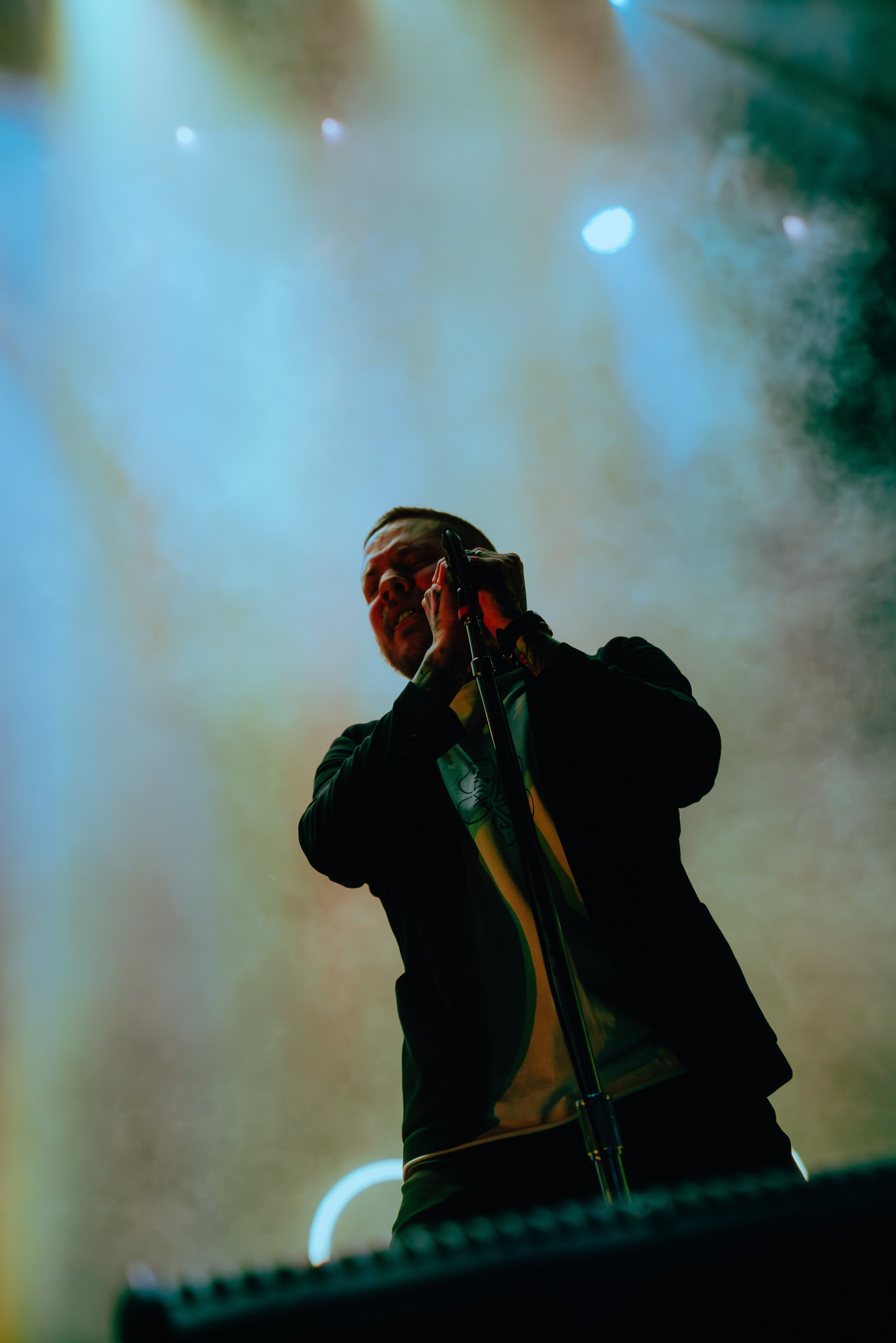 Male singer performing on stage with colorful smoke and stage lights in the background.