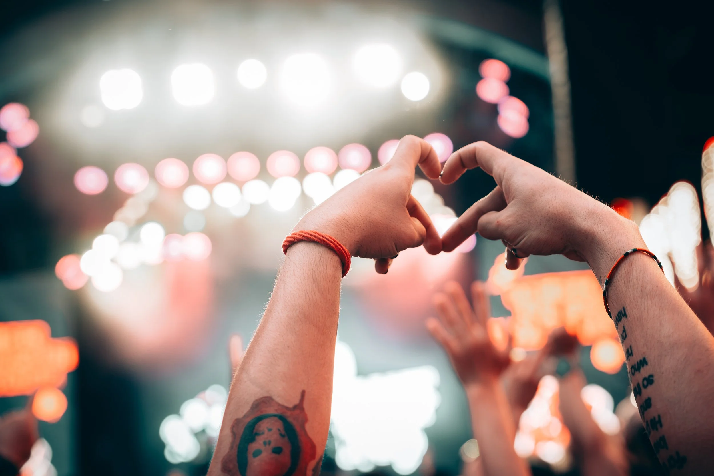 Two hands forming a heart shape against a blurred, colorful background of bright lights at night.