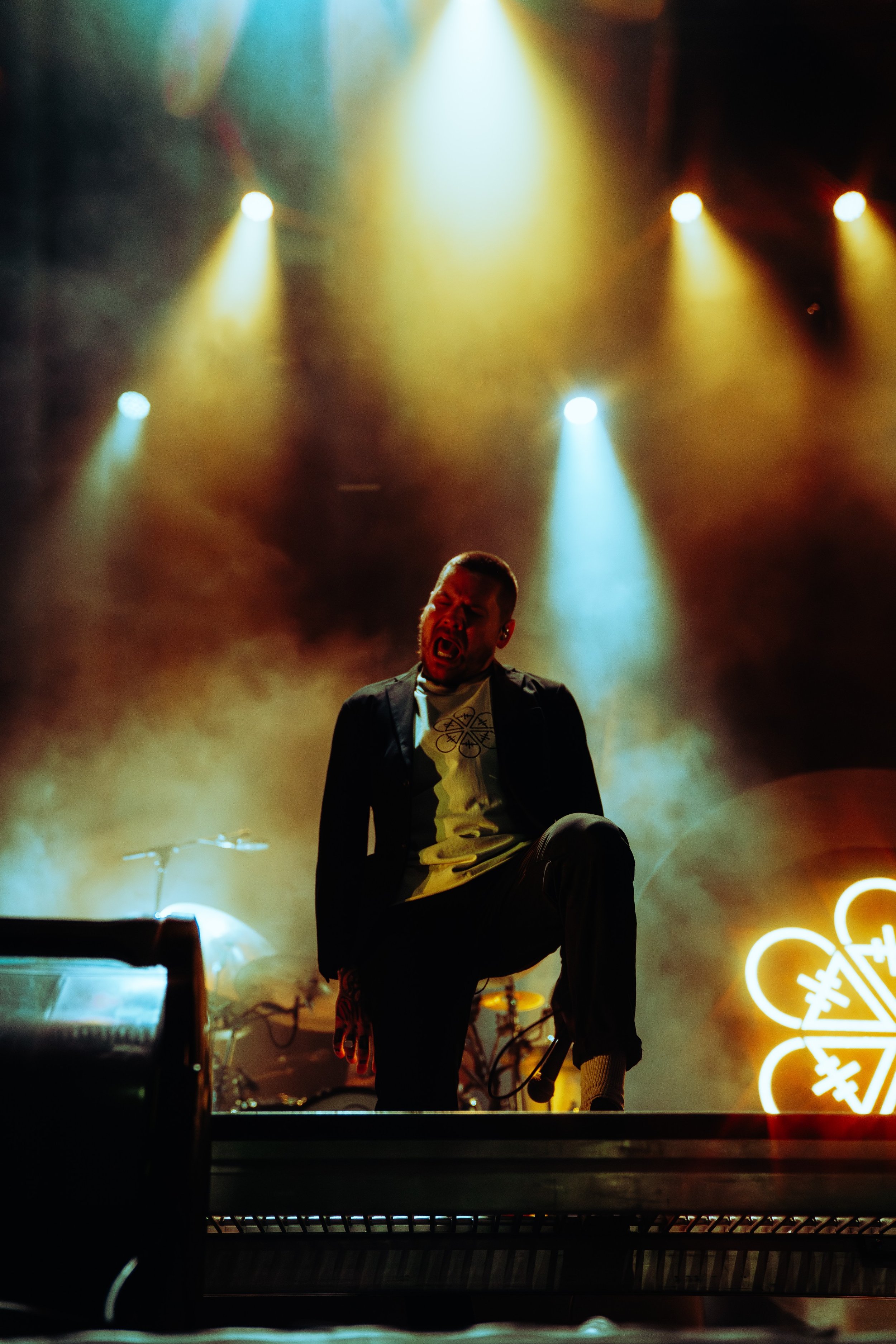 A singer on stage with colorful lights and smoke effects, performing passionately, with musical instruments and neon signs in the background.