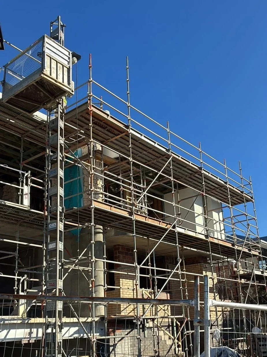 Construction site with scaffolding around a building under construction, against a clear blue sky.