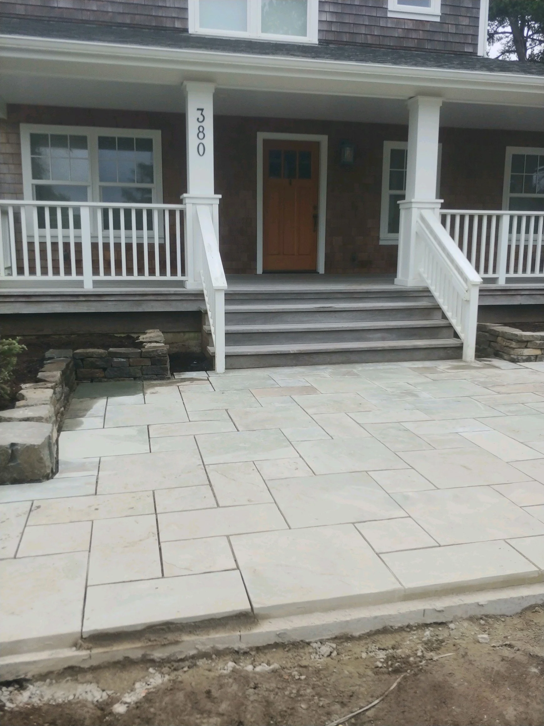 Front porch of a house with white railings and stairs, a wooden front door, and a brick exterior, with the house number 380 on a white pillar.