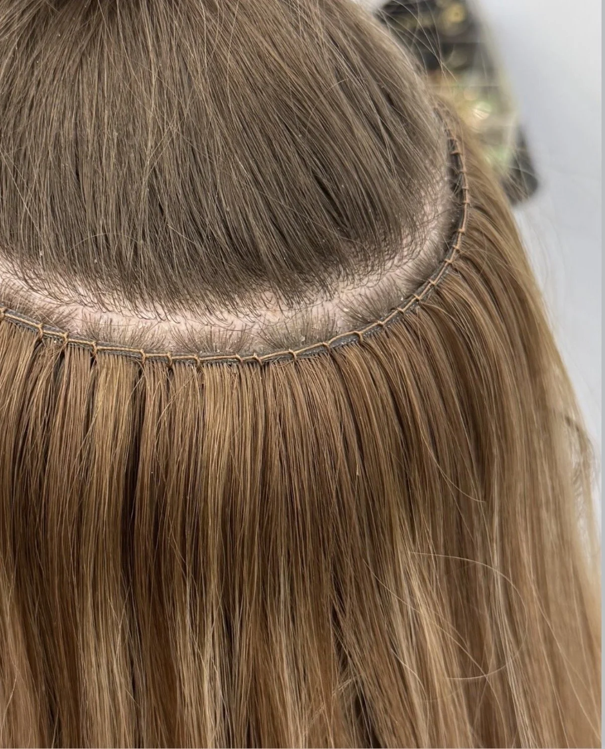 Close-up of a hair extension sewn into a weave, with hair parted and secured with a string.