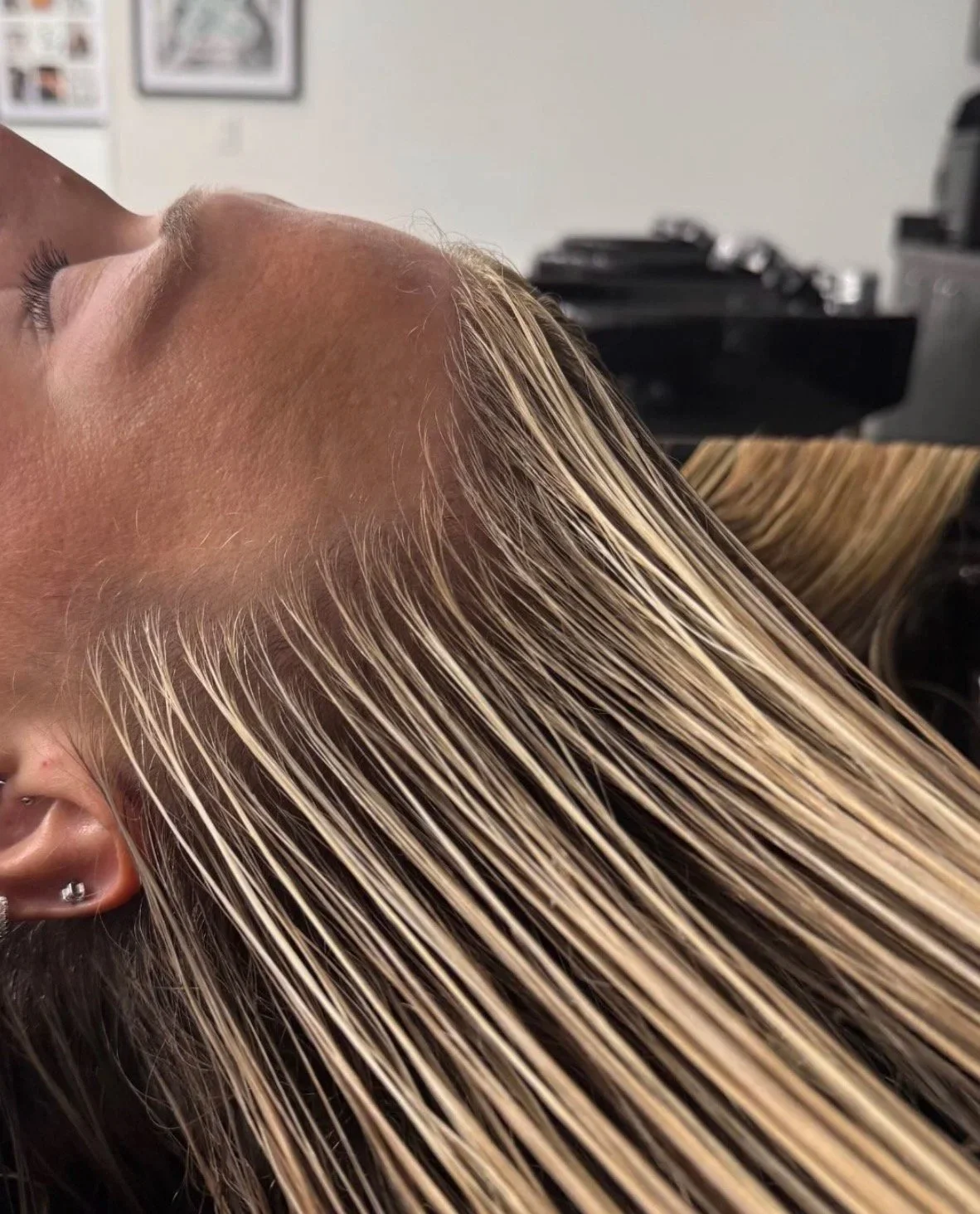 A person with blonde hair is lying back at a salon, receiving hair treatment, with their eyes closed.