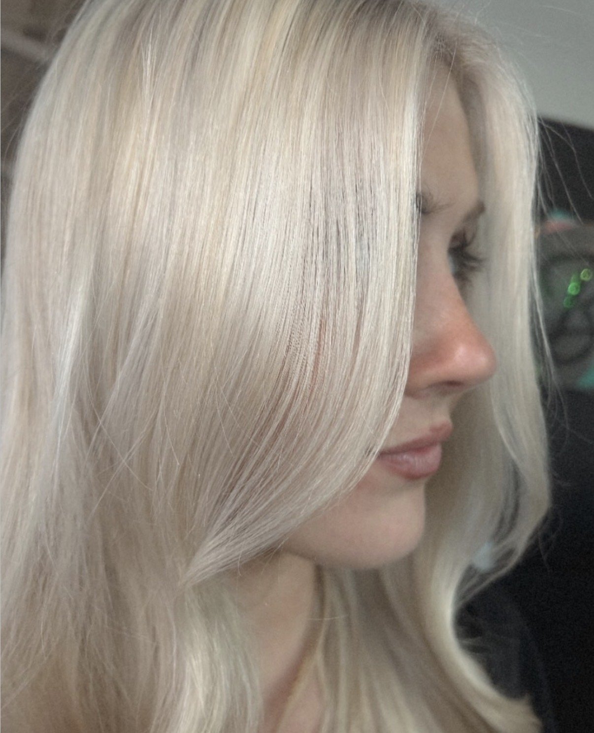Close-up side profile of a woman with long, straight, platinum blonde hair.