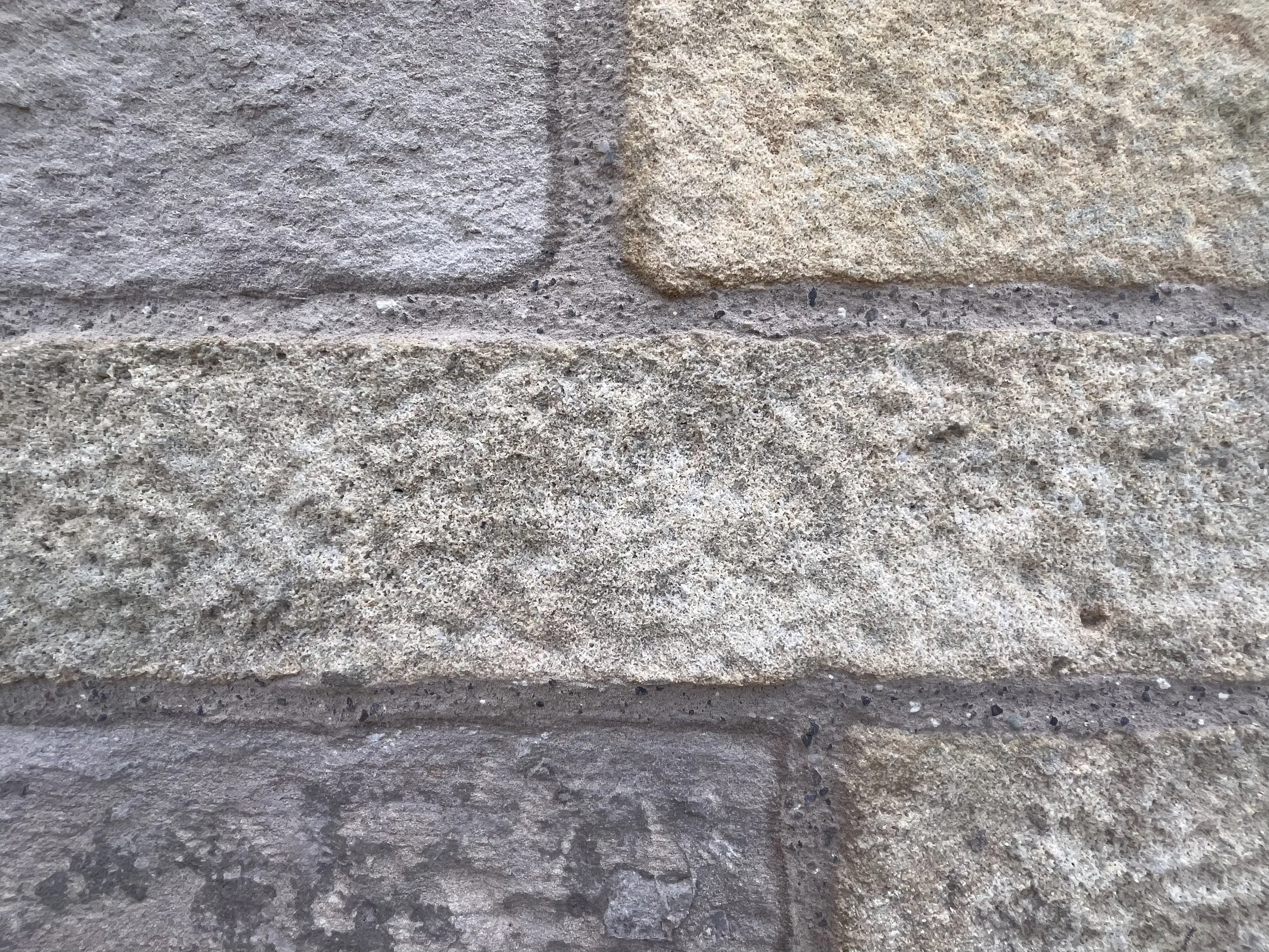Close-up image of a brick wall with textured, rough, grayish and tan-colored bricks.
