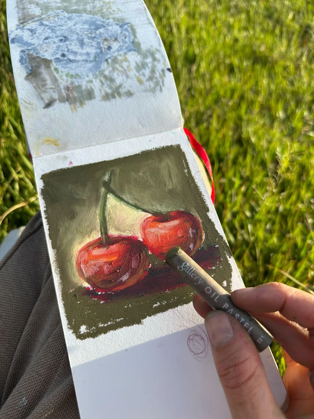 El dibujo de dos cerezas rojas con hojas verdes, pintado con óleo, sobre una superficie de fondo oscuro.