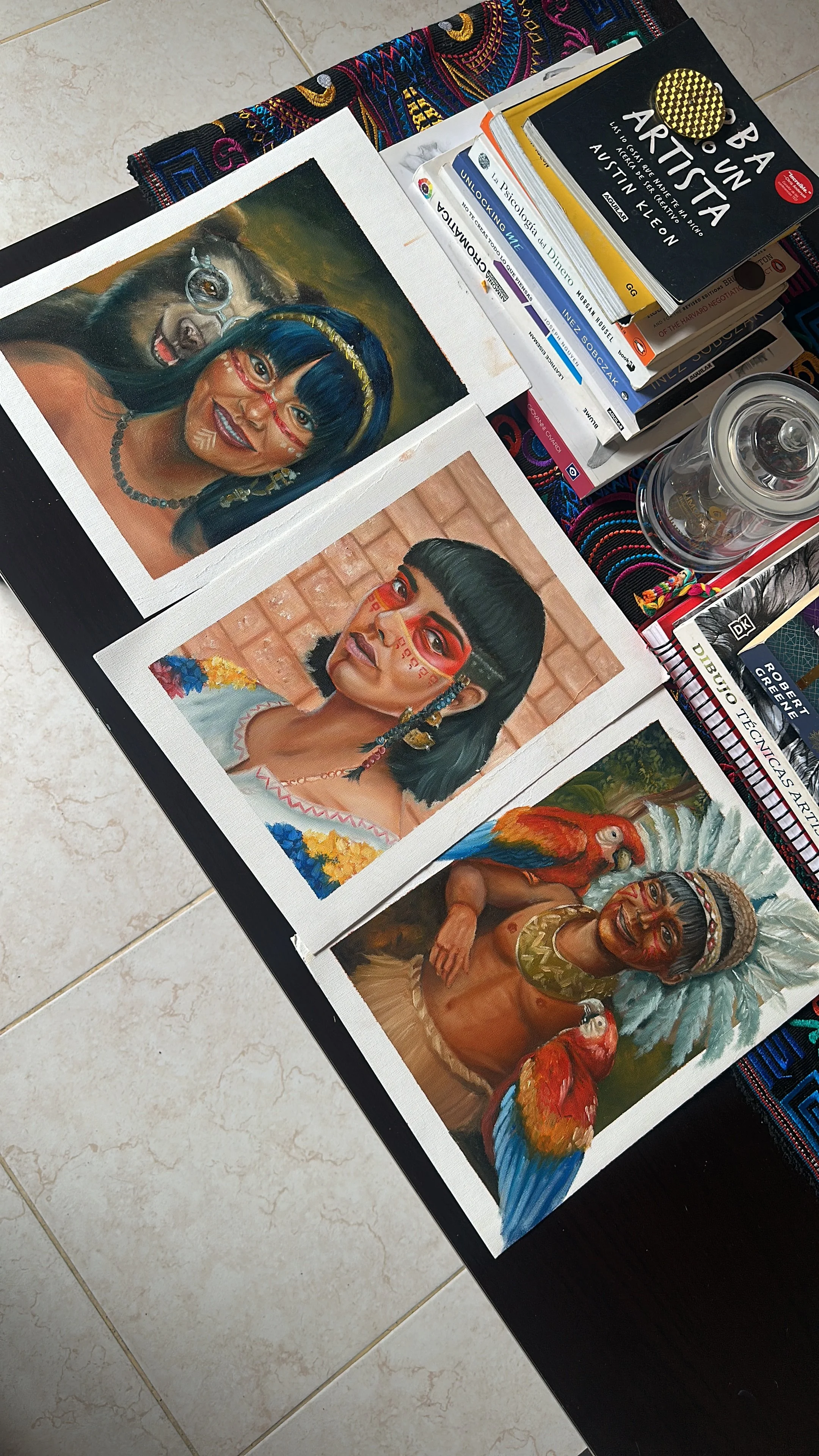 Tres retratos de personas indígenas con maquillaje facial y adornos en un estilo tradicional, acompañados de un loro y un guacamayo, en una mesa con libros y objetos decorativos.