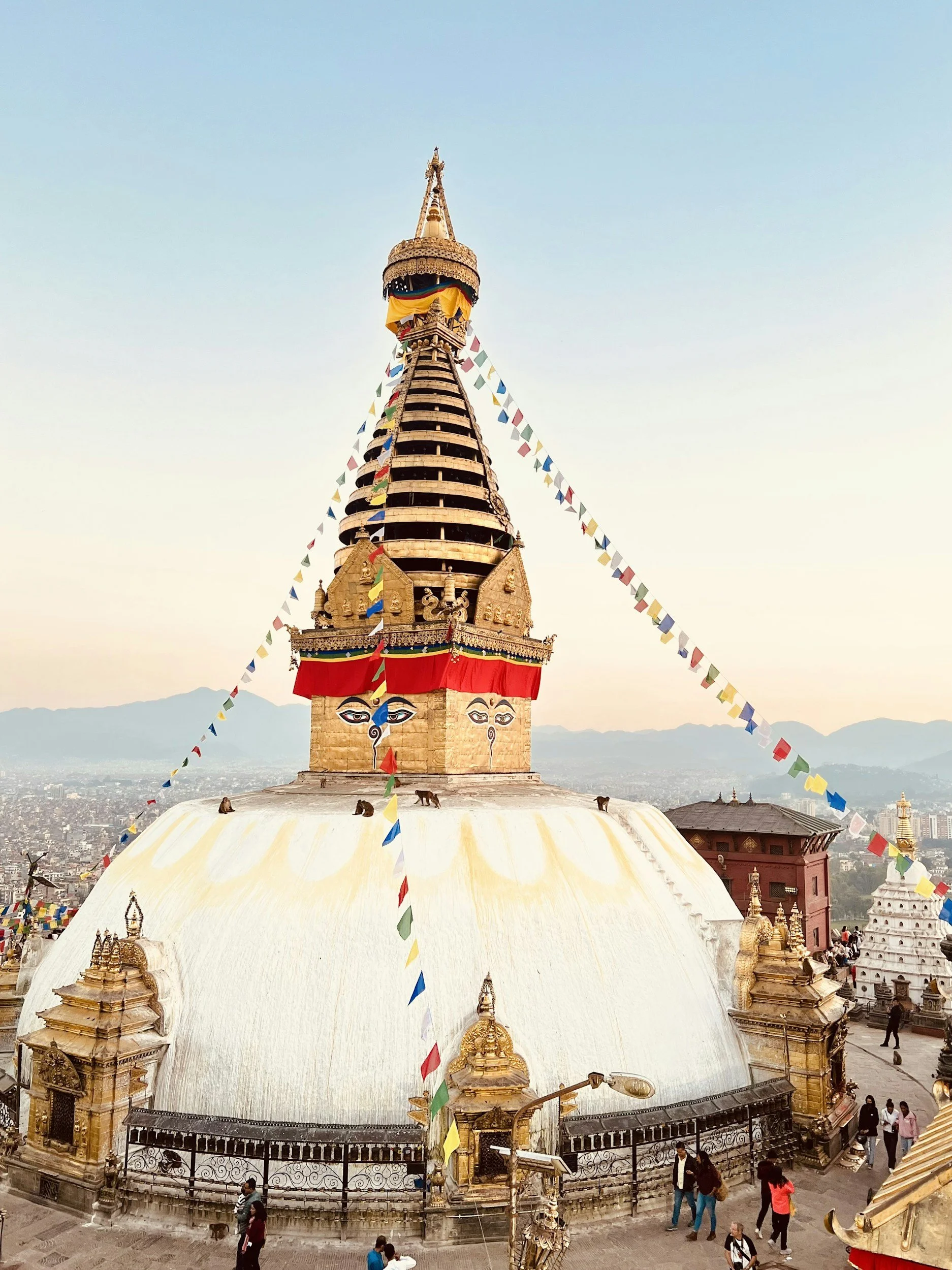 Vista de la cima del Stupa de Swayambunath en Katmandú, Nepal, con una estructura dorada y banderas de oración colgadas.