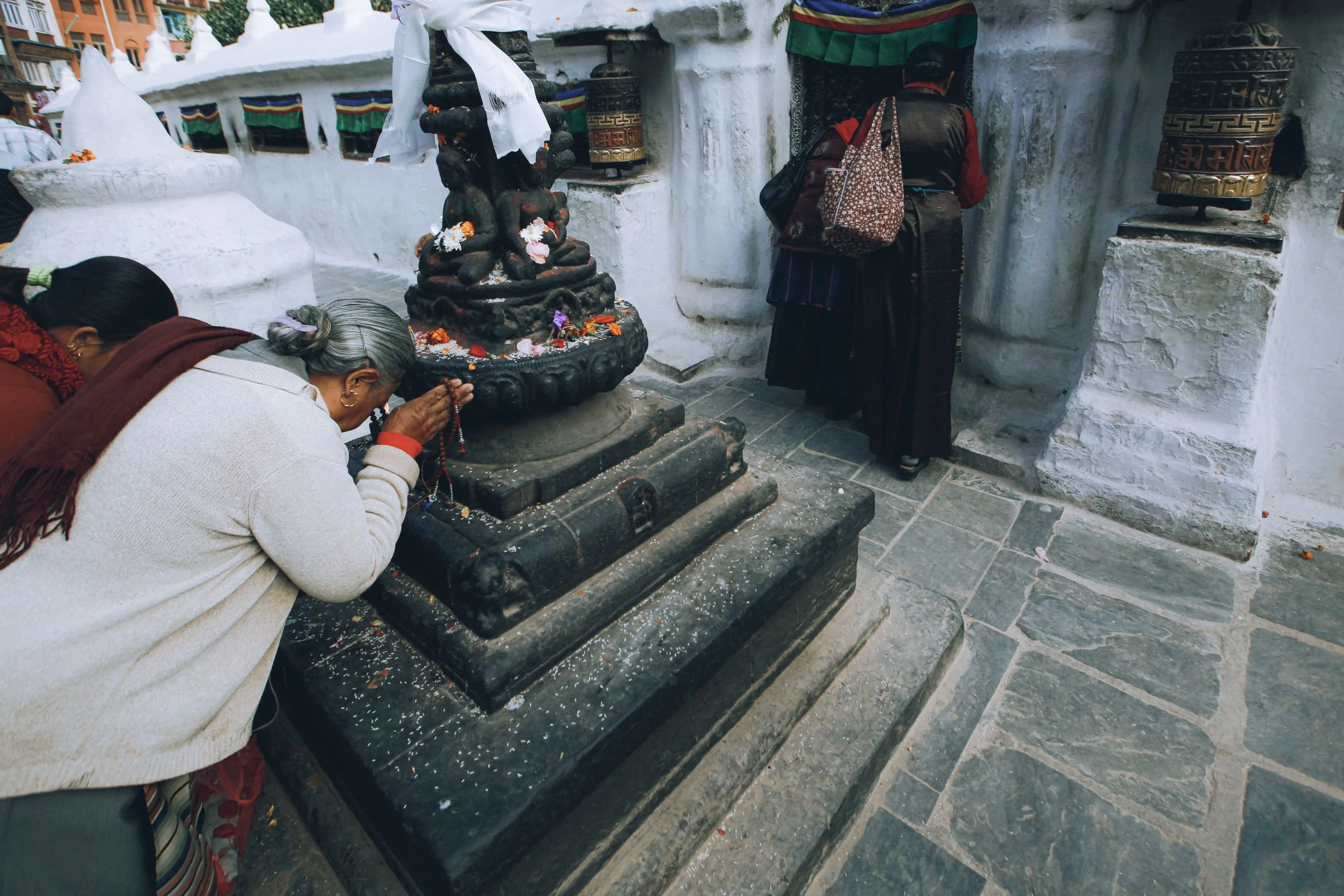 Personas frente a una estructura blanca con estatuas y banderas, realizando oraciones o rituales religiosos.