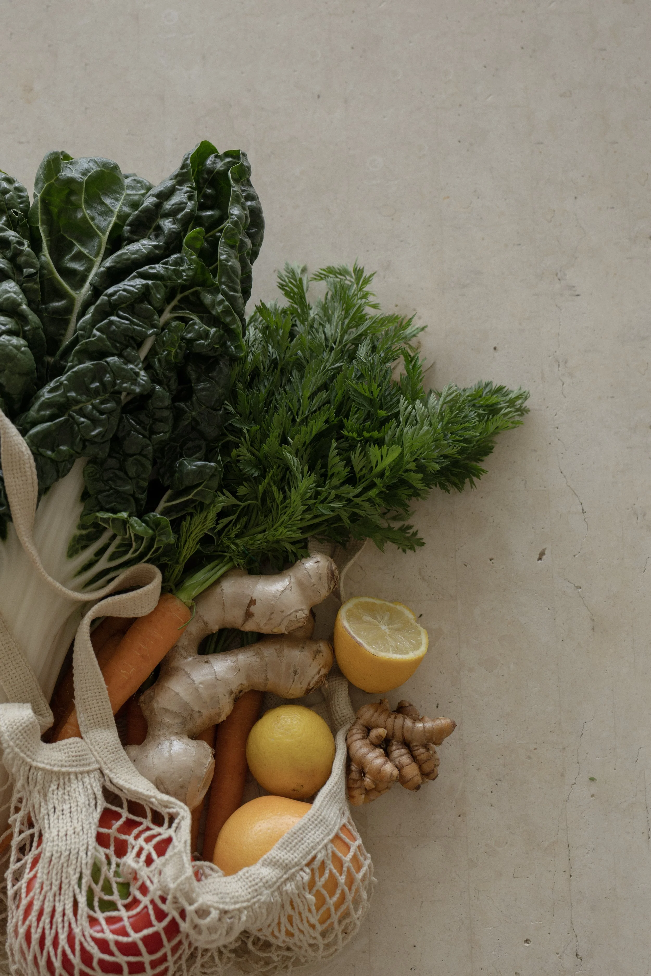 A collection of fresh vegetables and lemons in a reusable mesh bag on a light-colored surface.