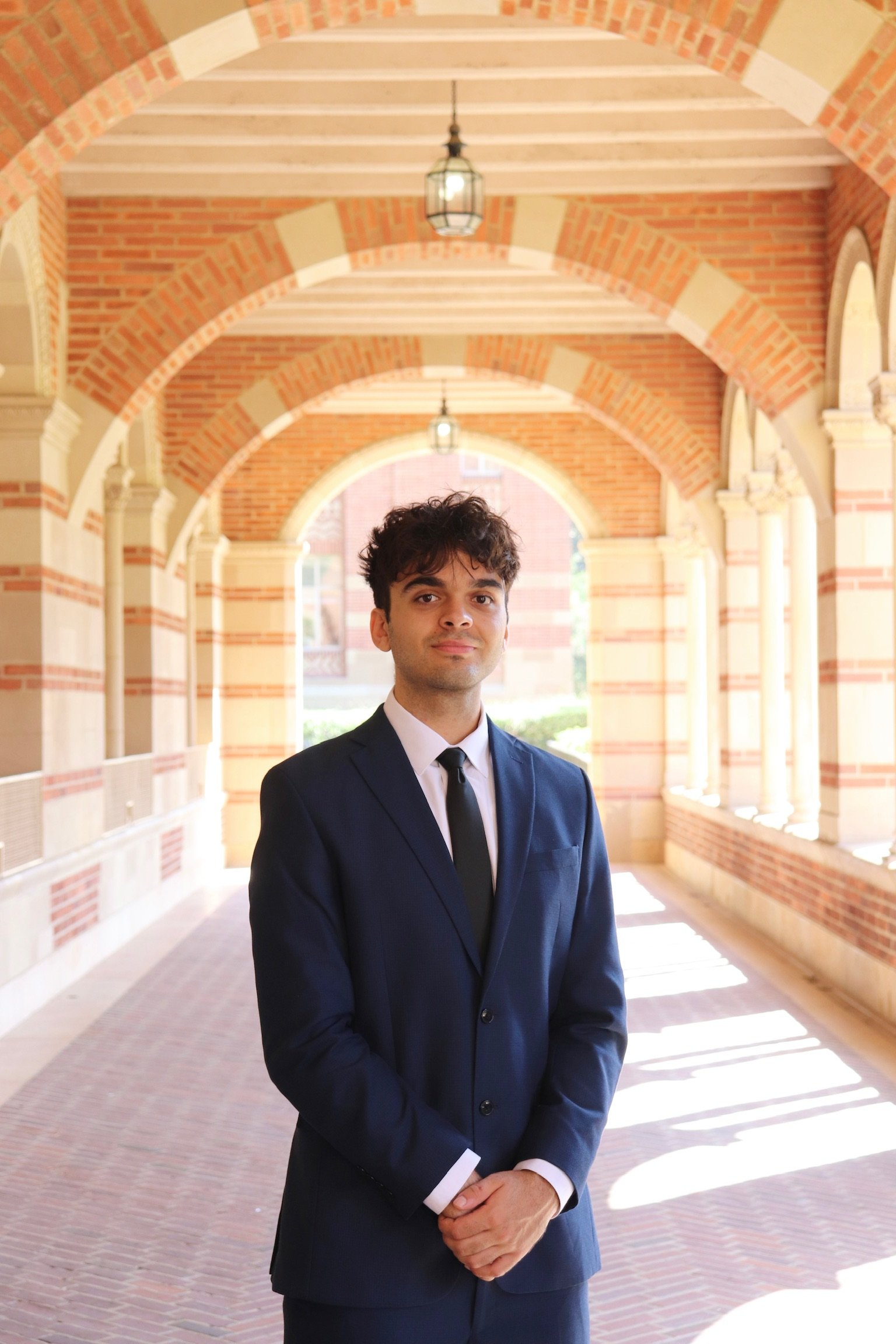 Portrait of Aren Khachaturian in a suit, standing in a brick archway