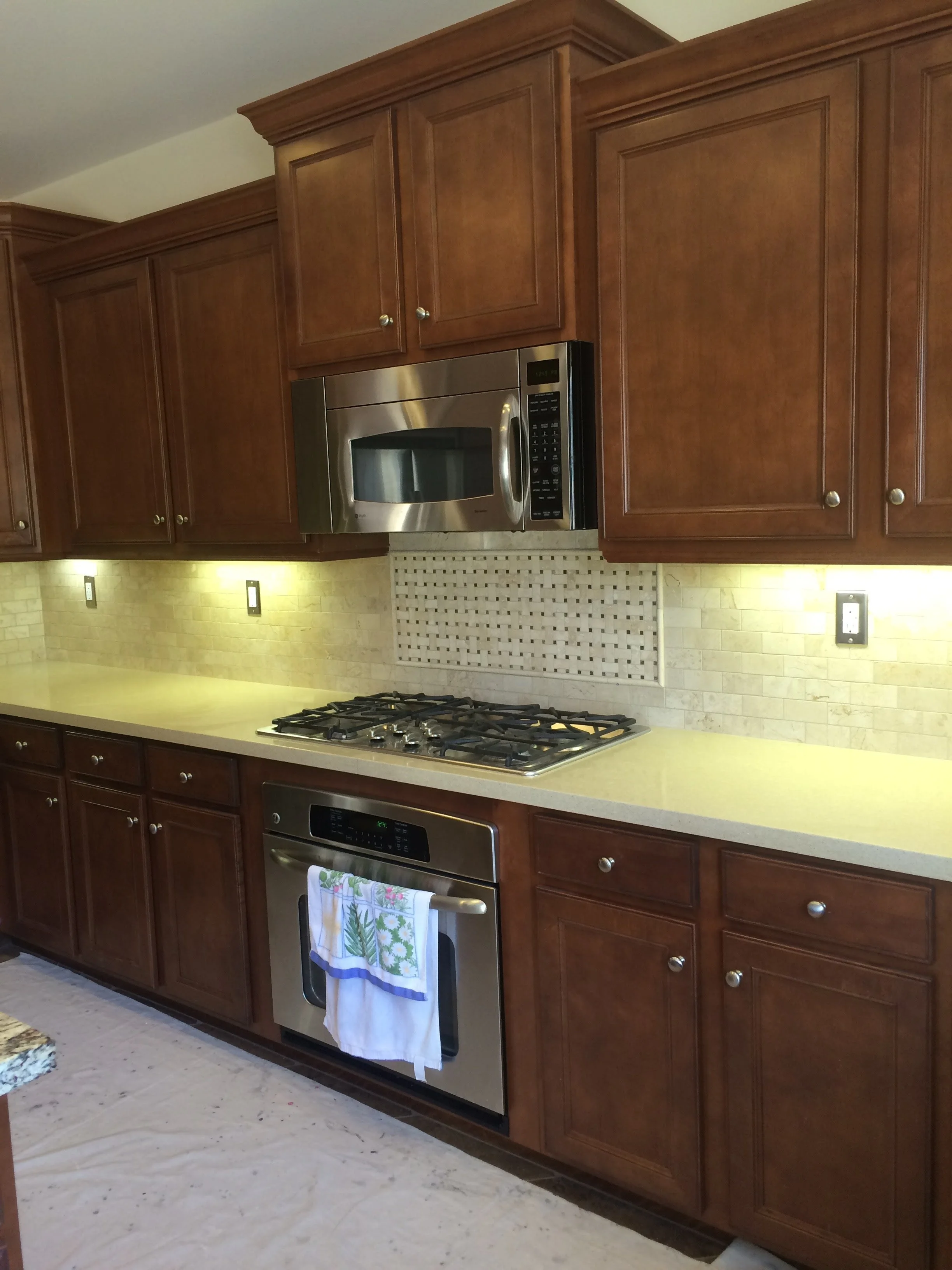 Kitchen with wooden cabinets, stainless steel microwave above a gas stove, light-colored counter, and a stove with a towel hanging on the handle.
