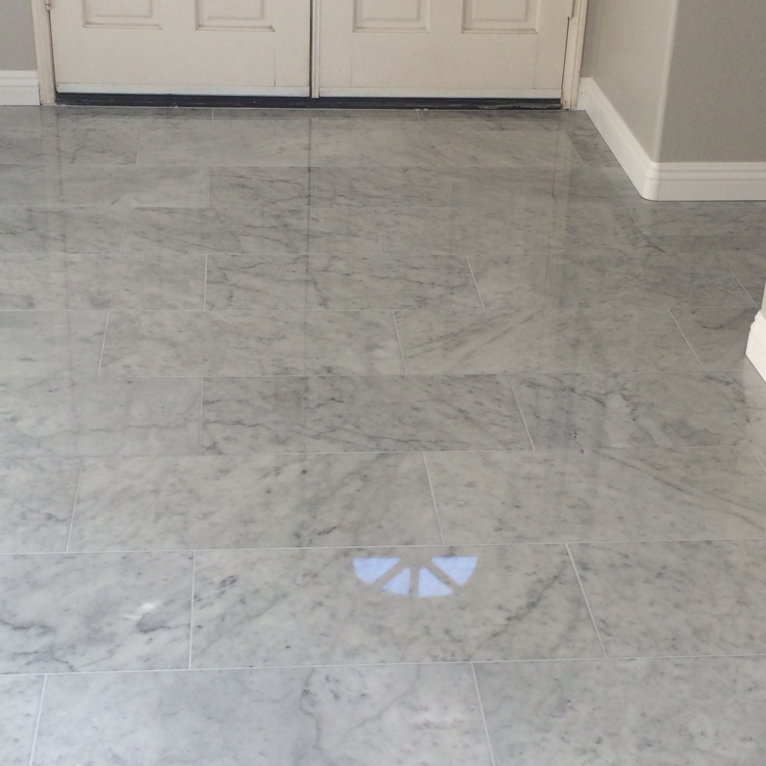 View of marble floor with a door in the background and a reflection of a window or light on the floor.