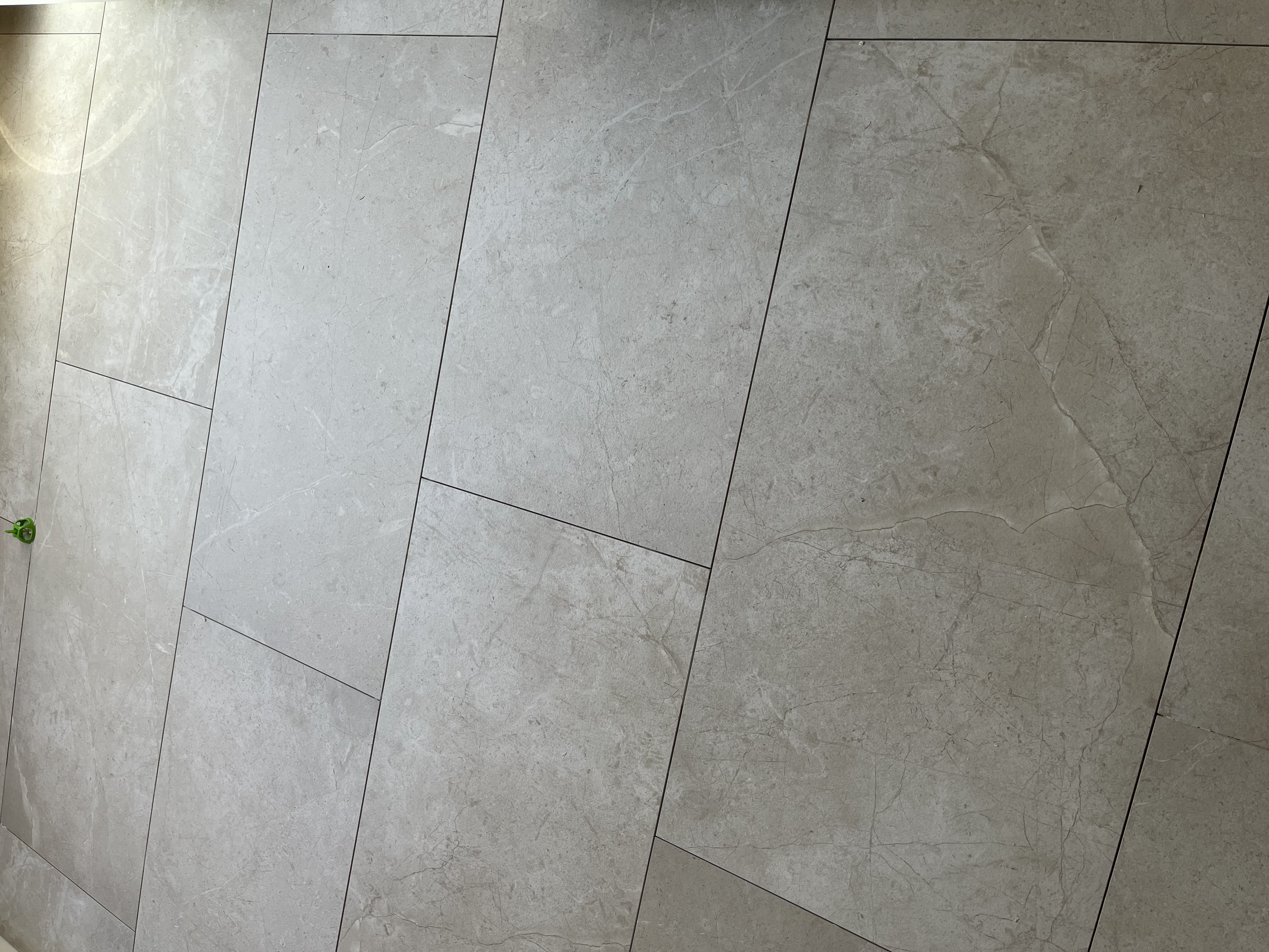 A tiled floor with light gray tiles and a small green object near the top center.