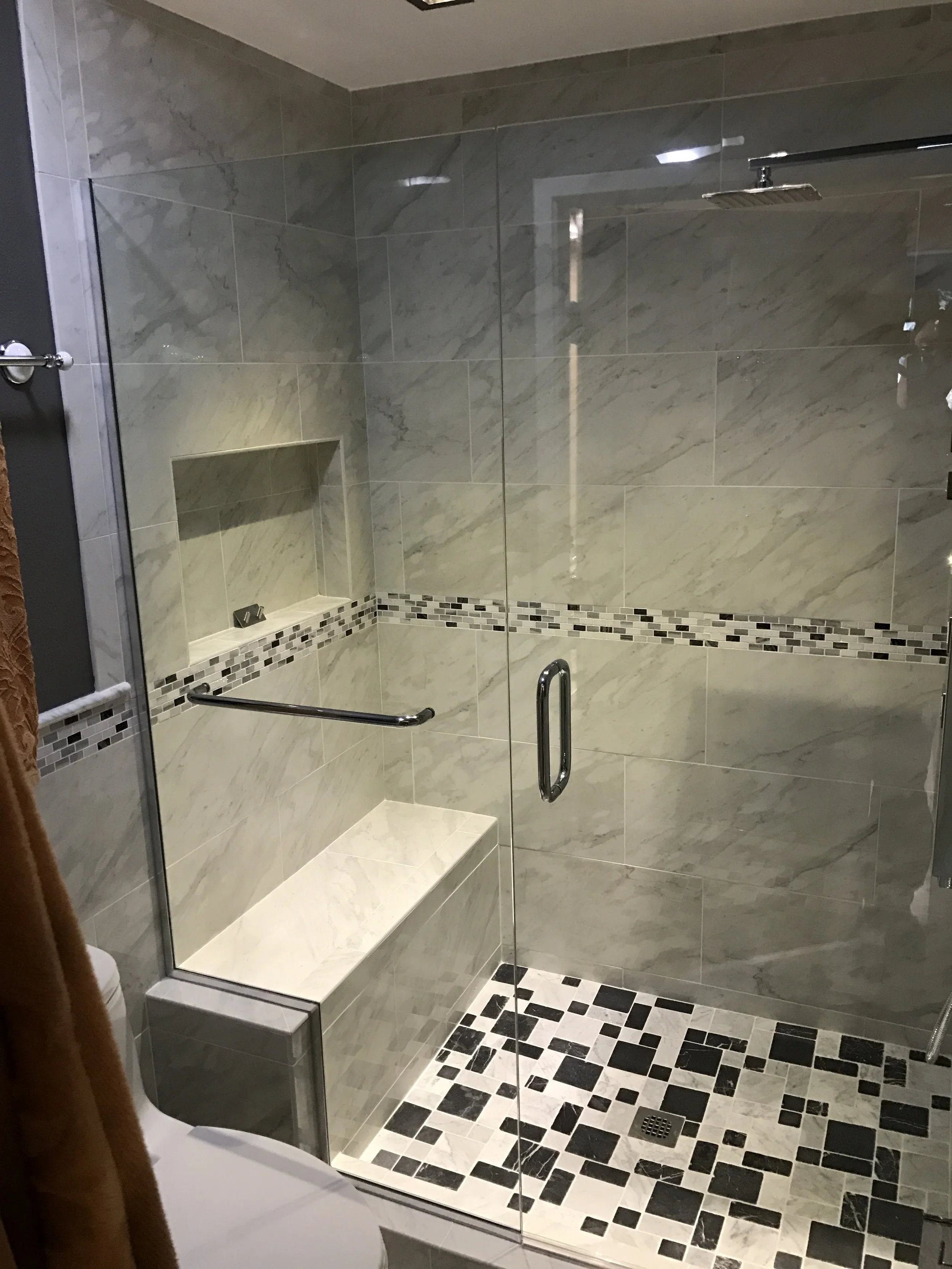 A modern walk-in shower with glass walls, gray marble tiles, a built-in shelf, a rain showerhead, and a black and white tiled floor.