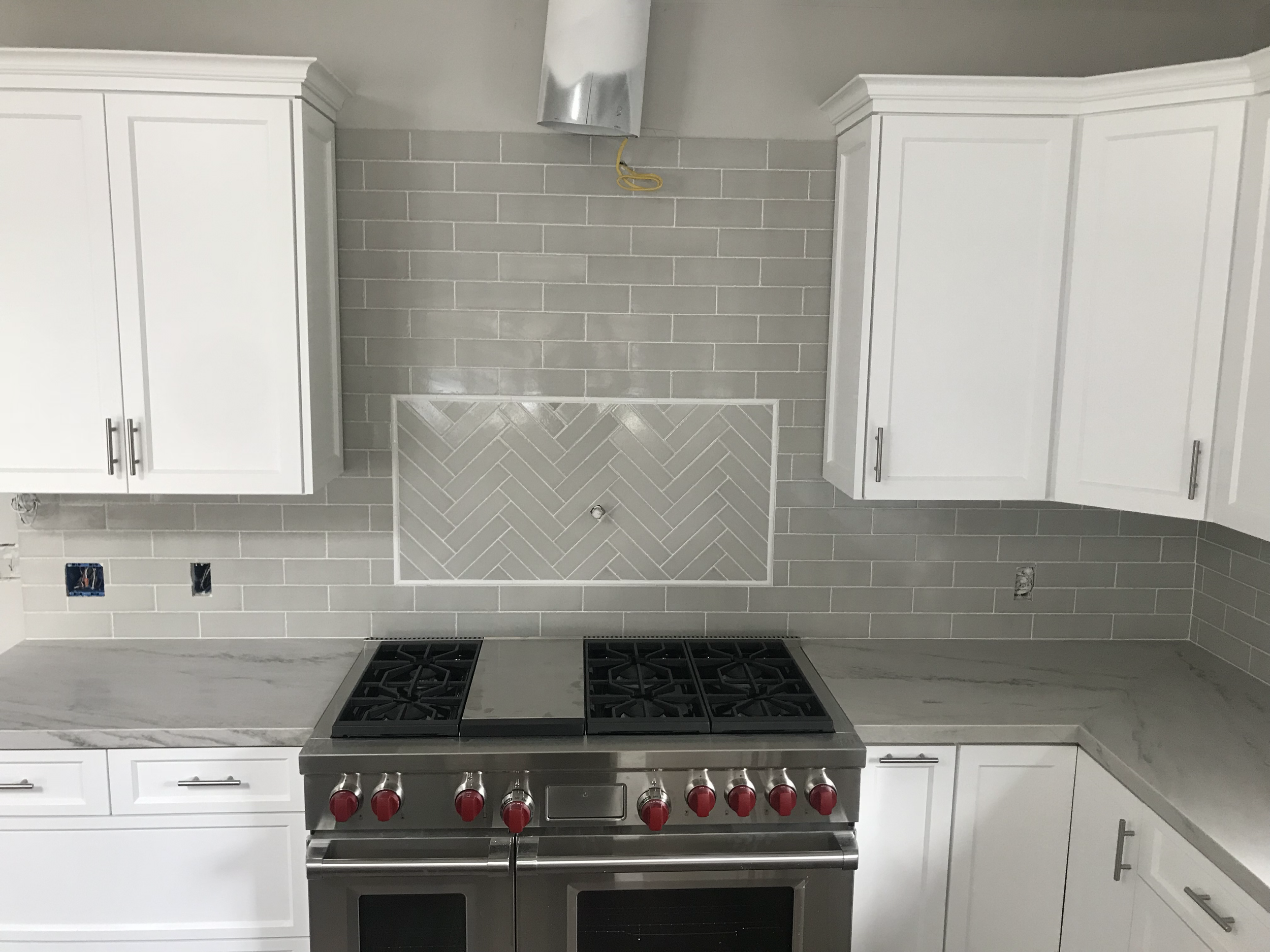 Newly installed kitchen with white cabinets, a gray backsplash, and a stainless steel gas range with red knobs.