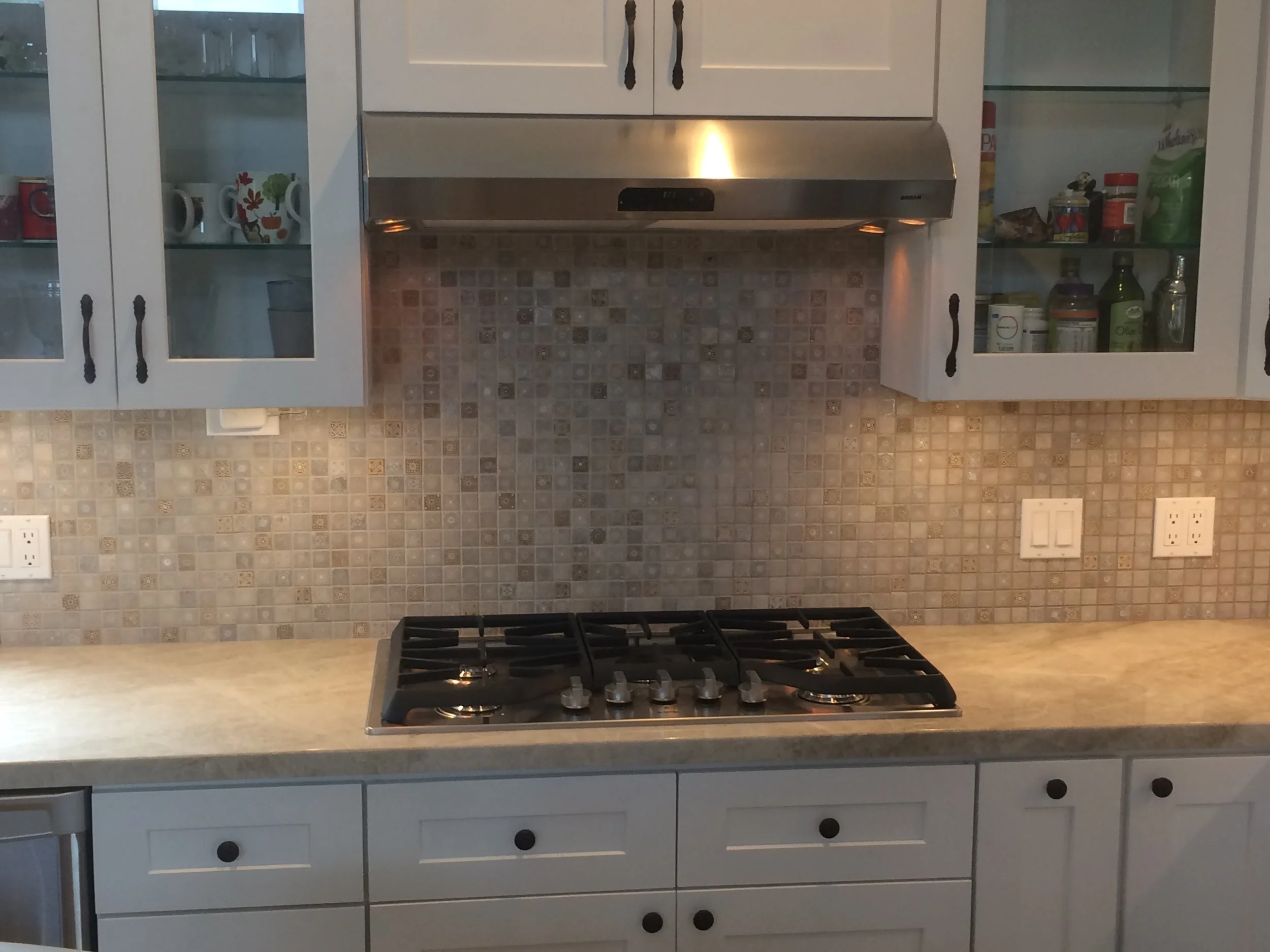 Kitchen with white cabinets, a tile backsplash, a stainless steel range hood, and a gas cooktop.