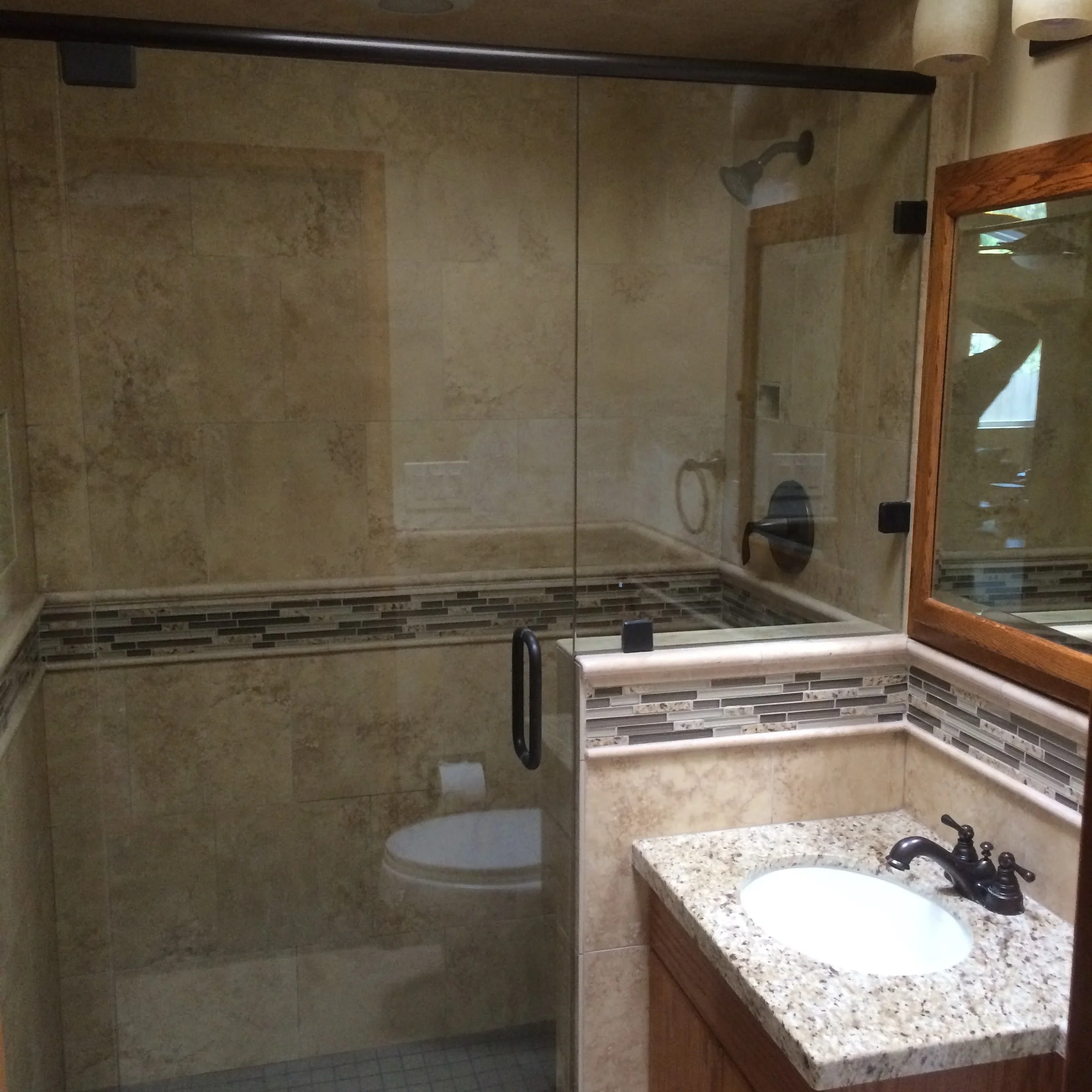 Bathroom with a glass shower enclosure, a granite countertop with a sink, a wooden mirror, and a chair near the shower.