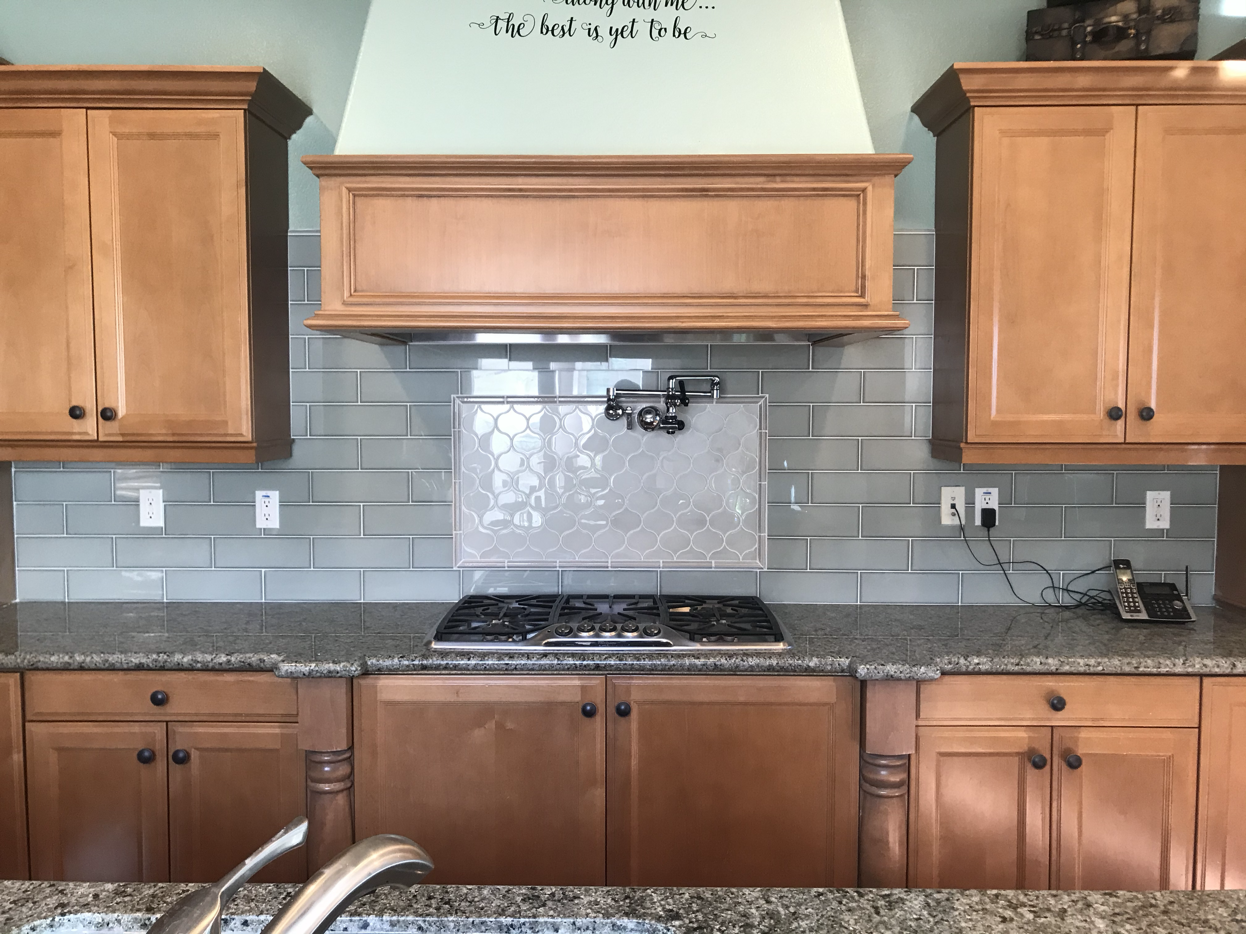 Kitchen backsplash with white subway tiles, wooden cabinets, granite countertop, gas stove, and a black telephone on the counter.