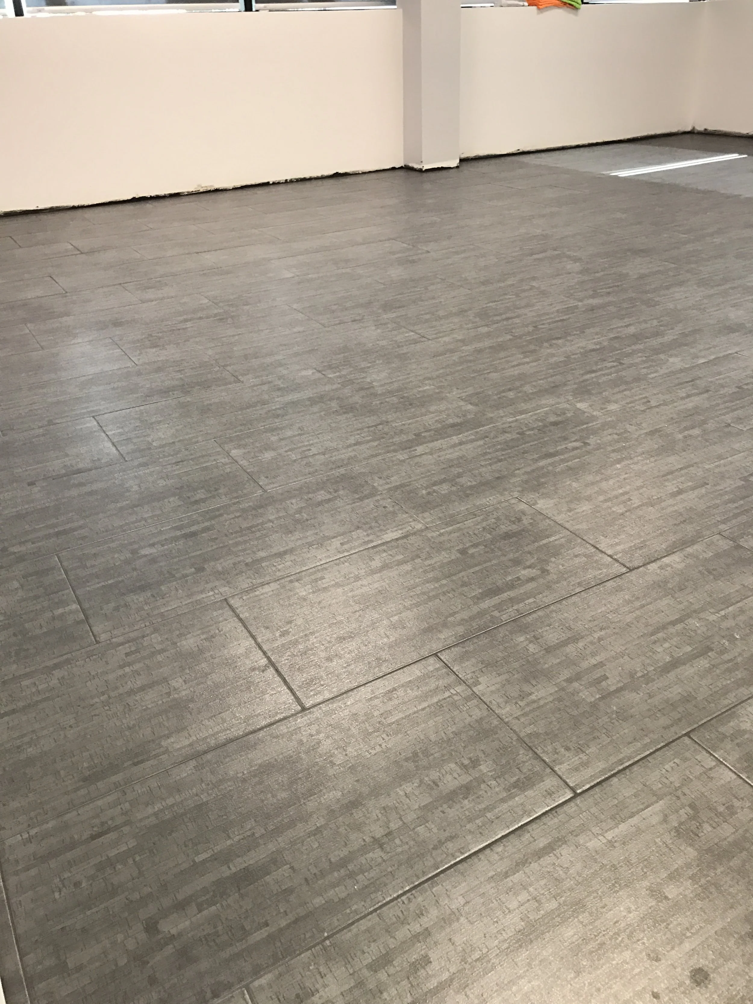 Gray tiled floor in front of beige wall with some colorful objects partially visible at the top of the image.