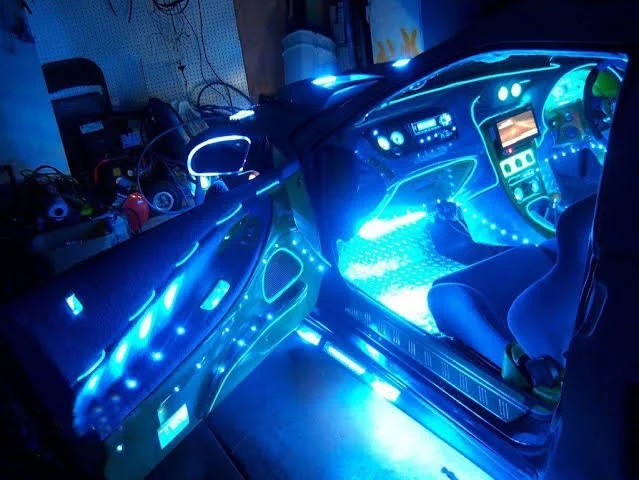 Inside a car with illuminated blue LED lights on the dashboard, door panels, and footwell, revealing a customized interior with a gaming or entertainment setup.