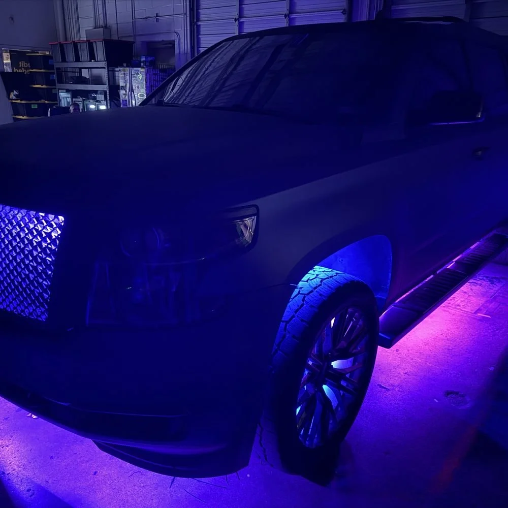 A dark-colored SUV with purple and blue underglow lights inside a garage or warehouse.