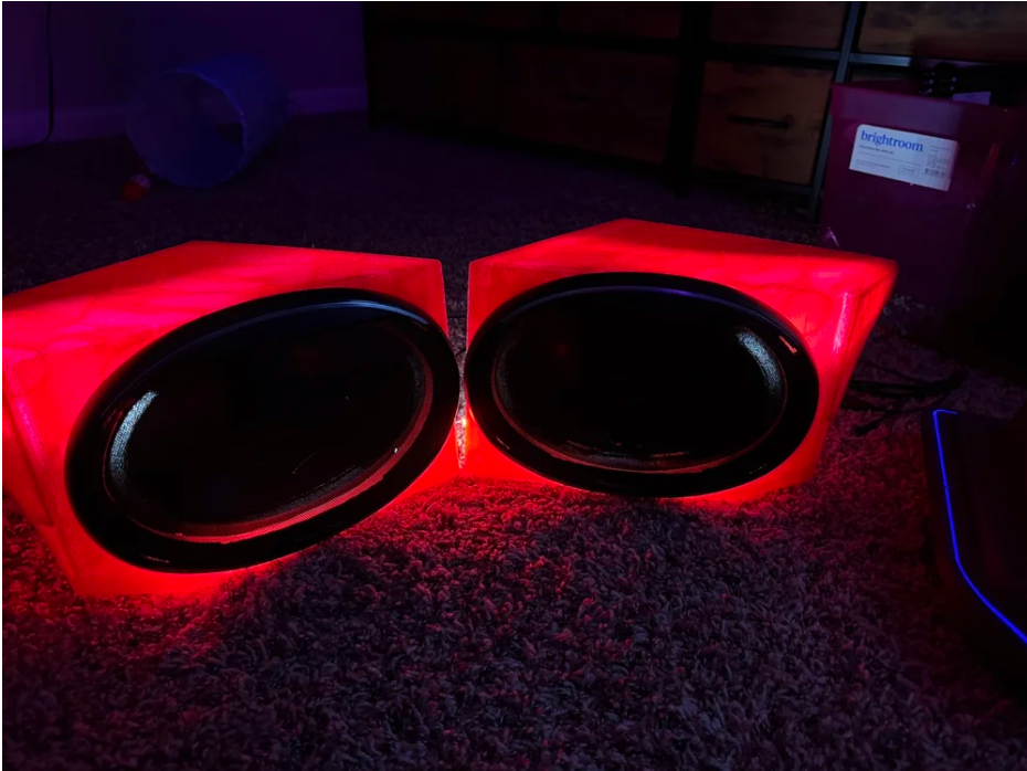 pair of illuminated red subwoofers on a carpeted floor in a dimly lit room.