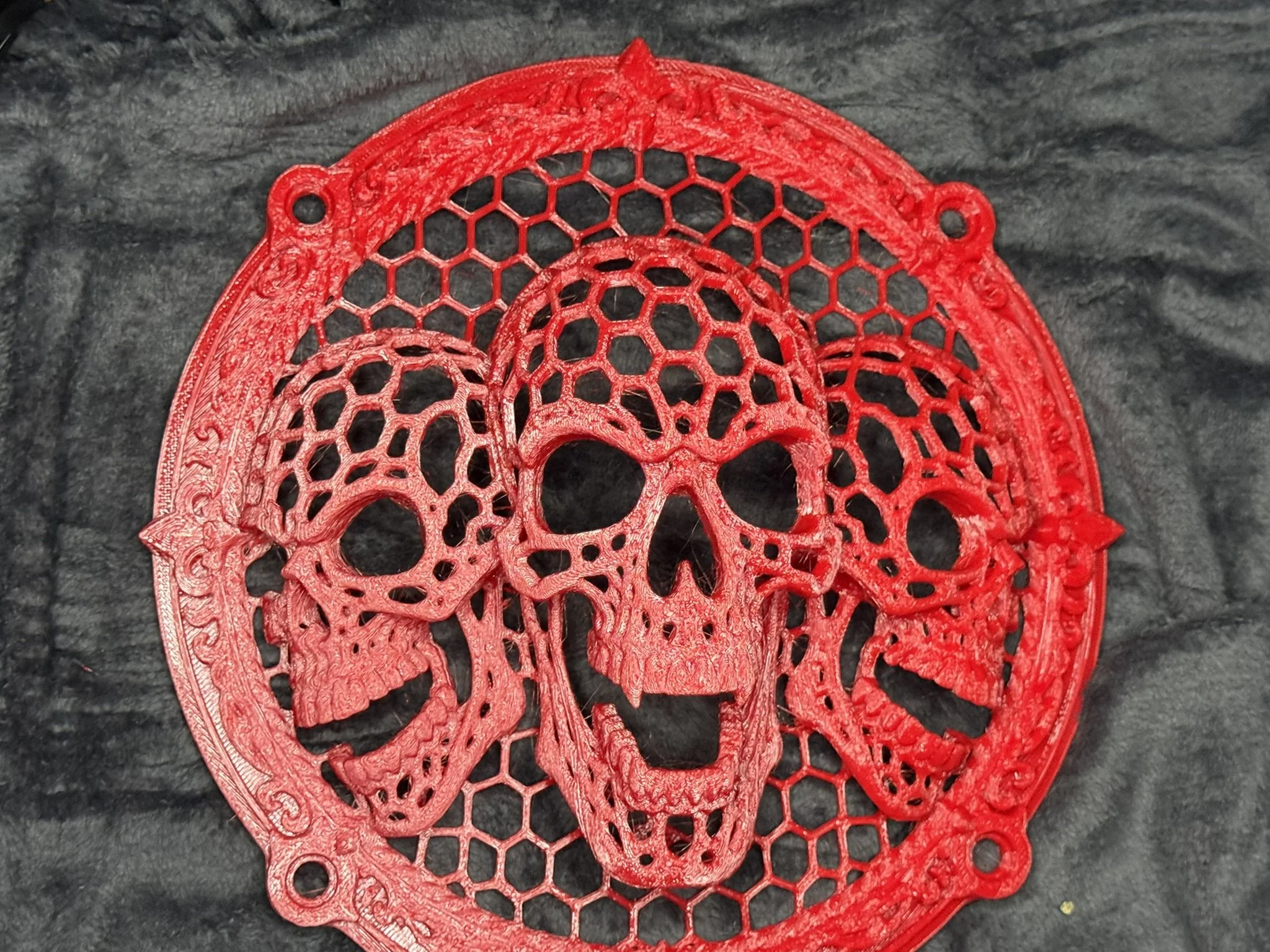 A close-up of red intricately designed lace or embroidery pieces with floral and circular patterns, placed on a dark textured fabric background.