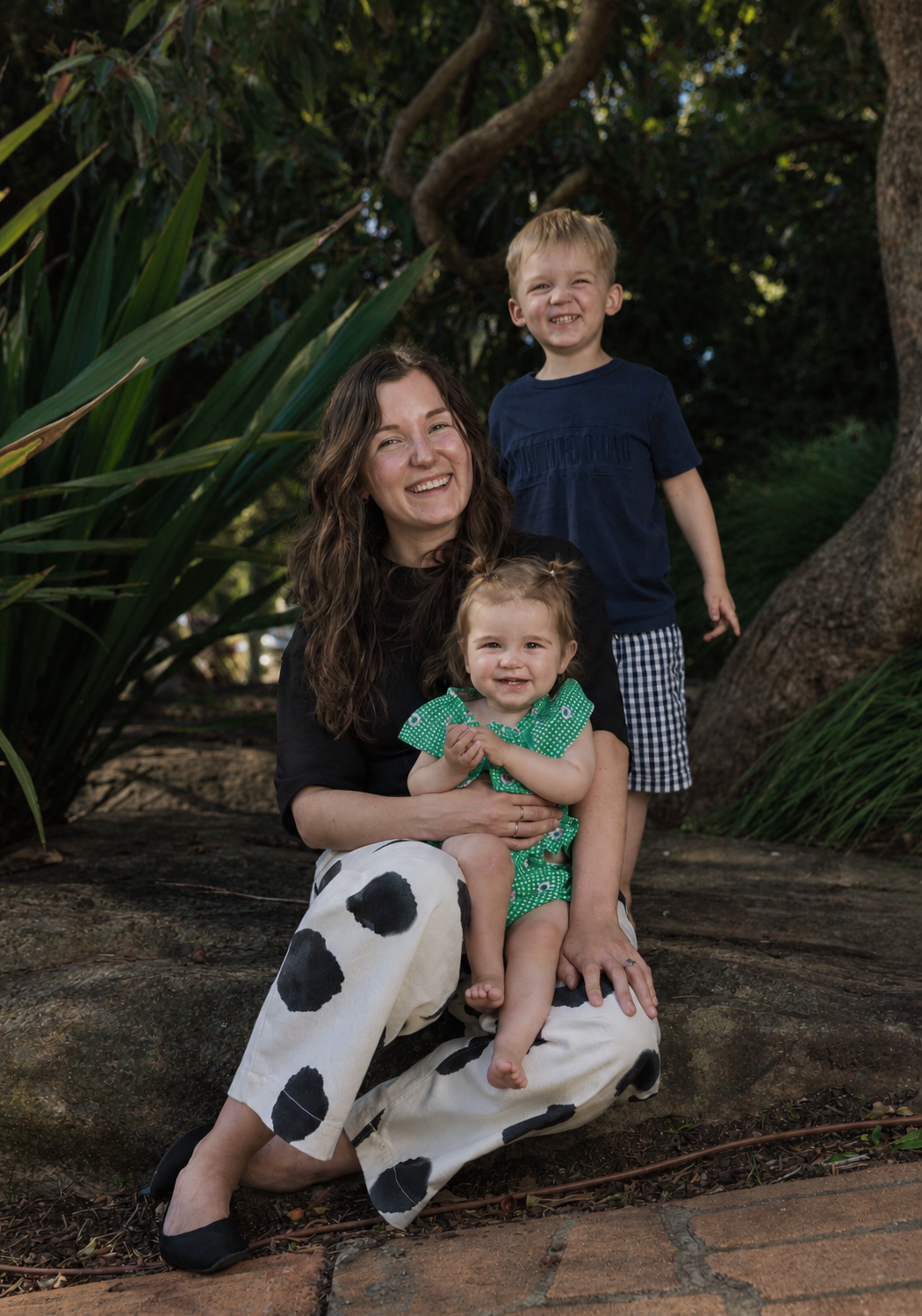 Bek Antognelli, founder of Brightside Buyers, sitting in a leafy garden with her two young children