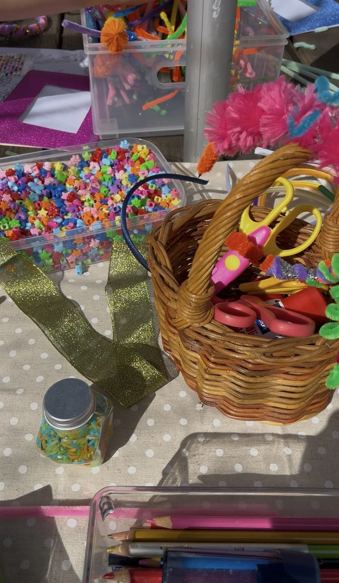 Colorful craft supplies including beads, pipe cleaners, scissors, and markers are arranged on a table at a craft event.