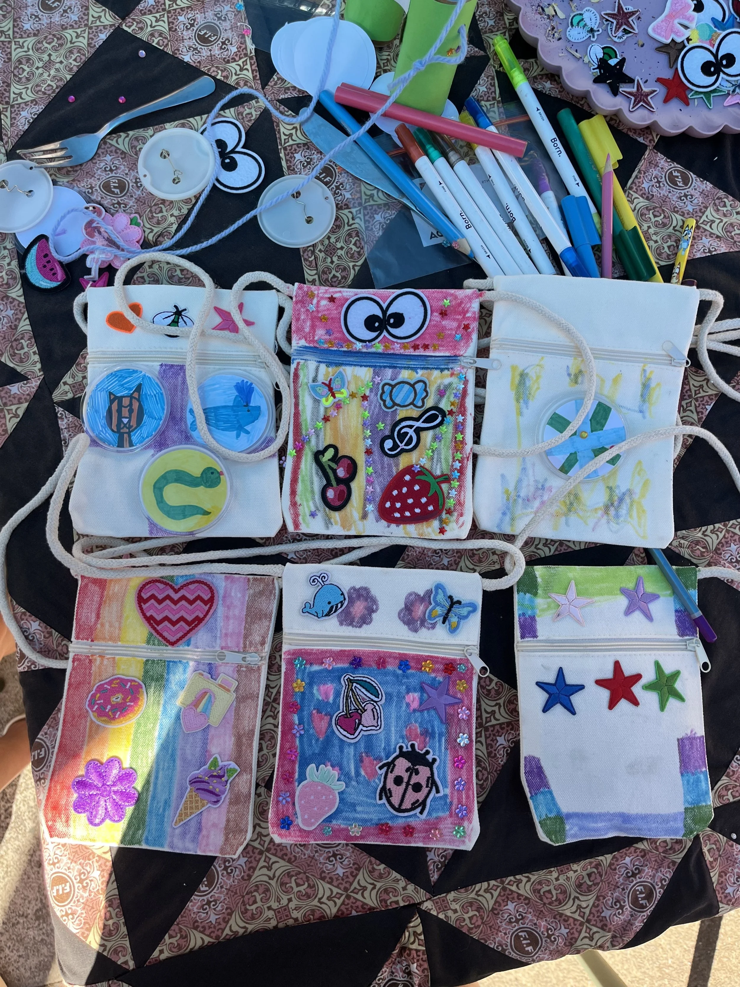 Colorful party favors and crafts, including decorated bags and stickers, arranged on a patterned tablecloth.
