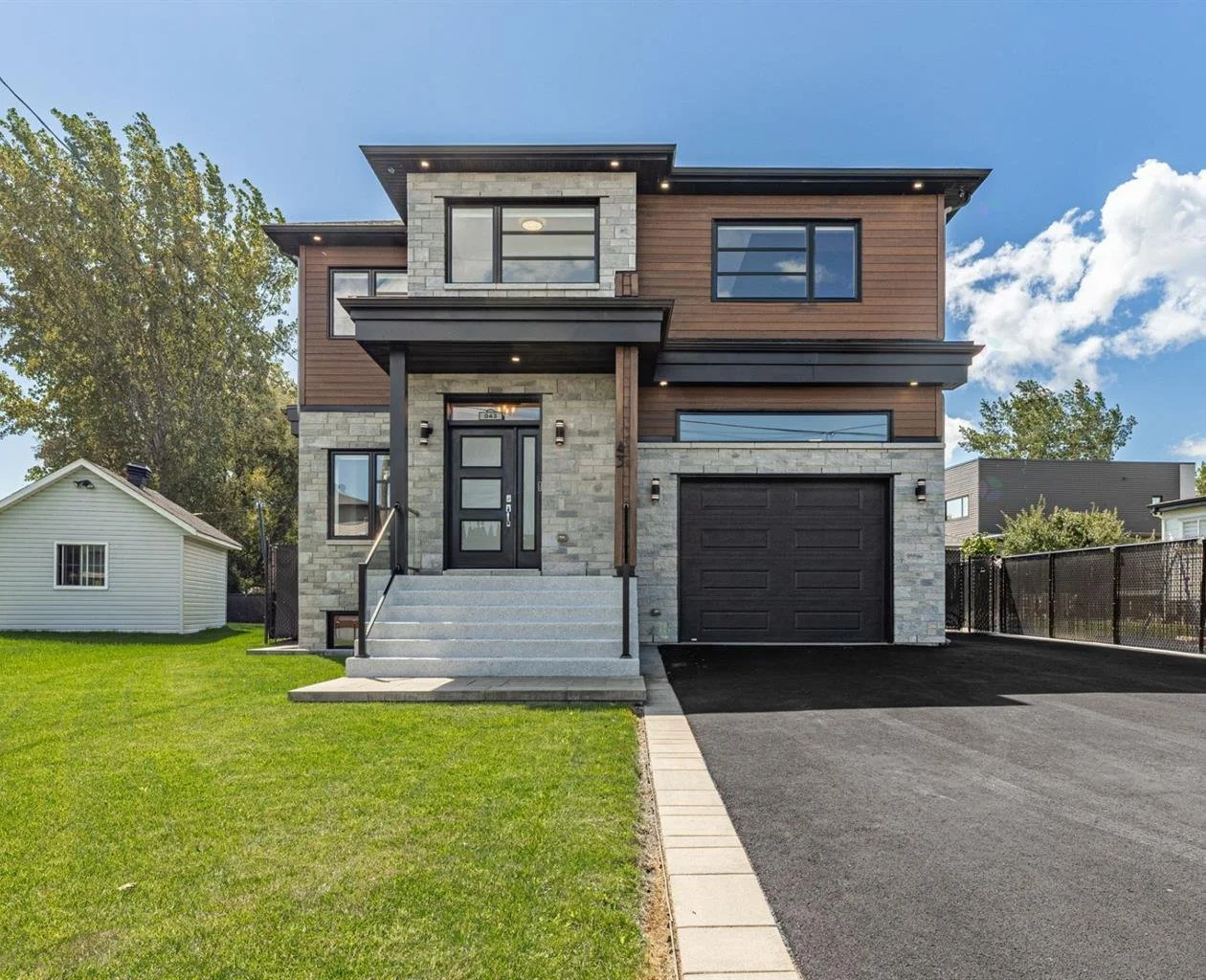 Modern two-story house with stone and wood exterior, black garage door, and front steps on a green lawn