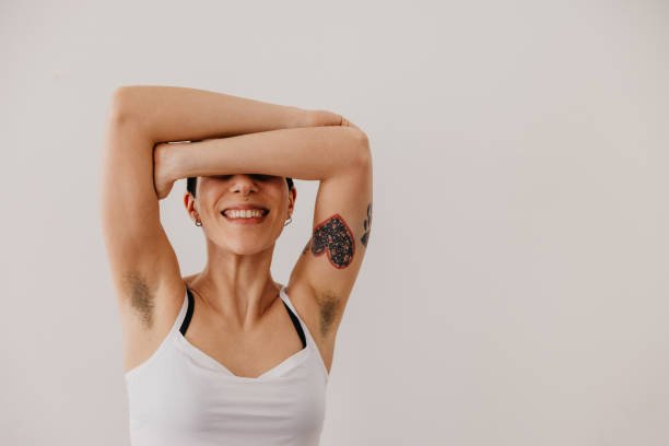 Woman smiling with her arms raised, representing professional underarm and body waxing services.