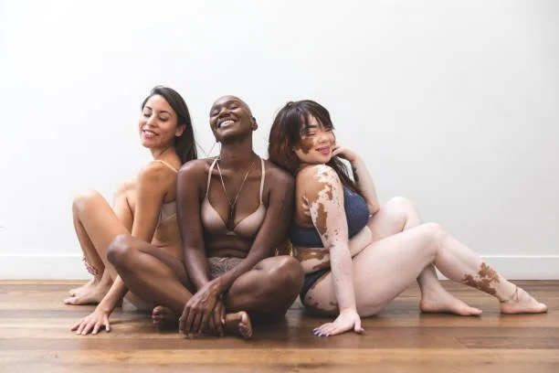 Three women sitting together, representing inclusive Brazilian and bikini waxing services for all body types.