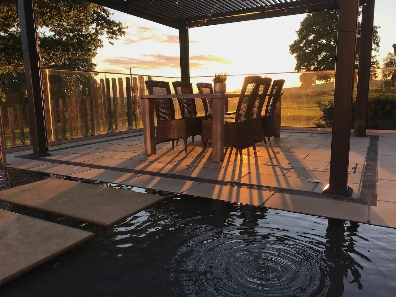 Evening sunlight falls across the sheltered dining terrace and reflecting water at The Paddocks.