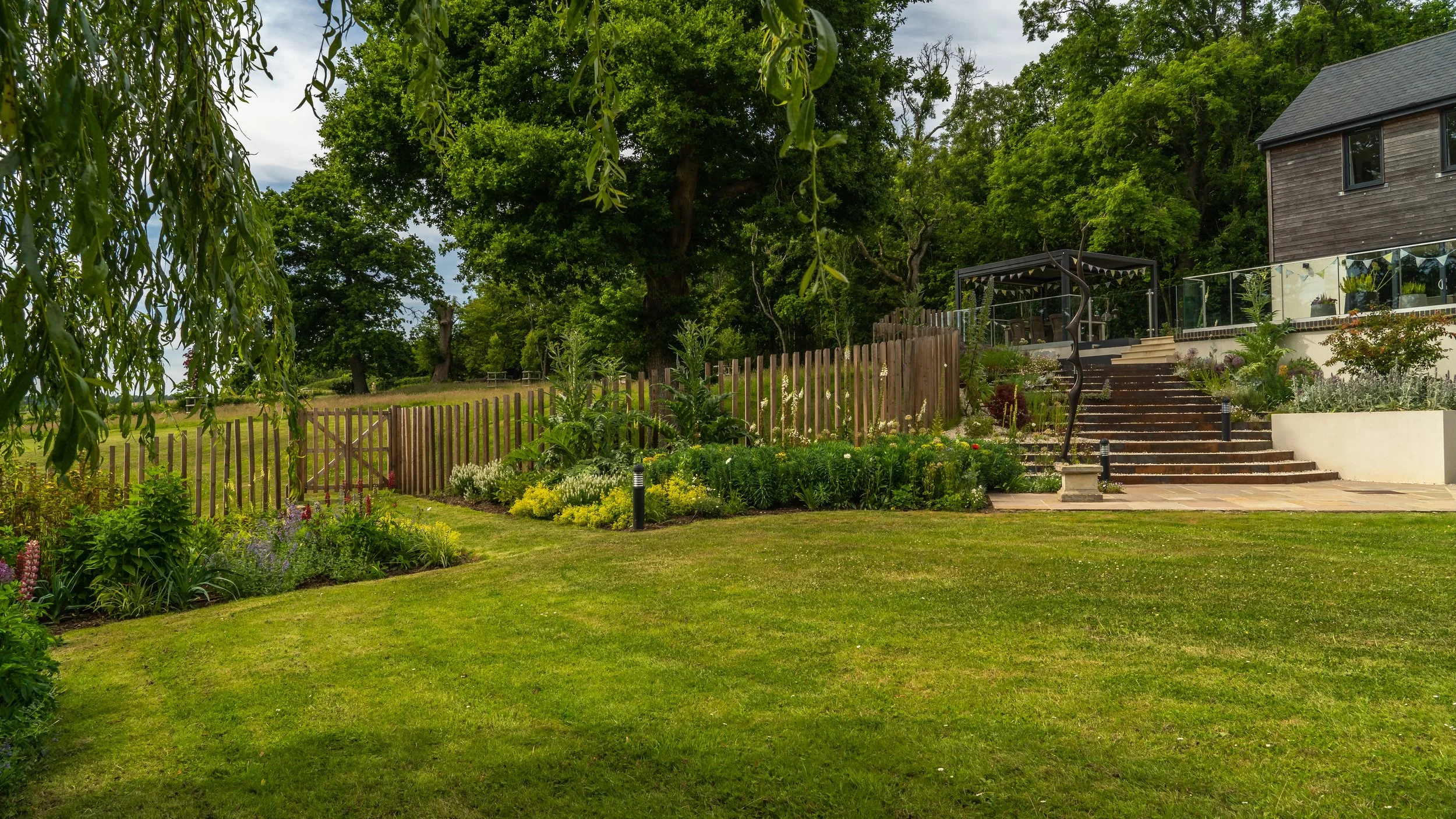 A wide view across the lawn and planted borders towards the terraces and steps at The Paddocks.