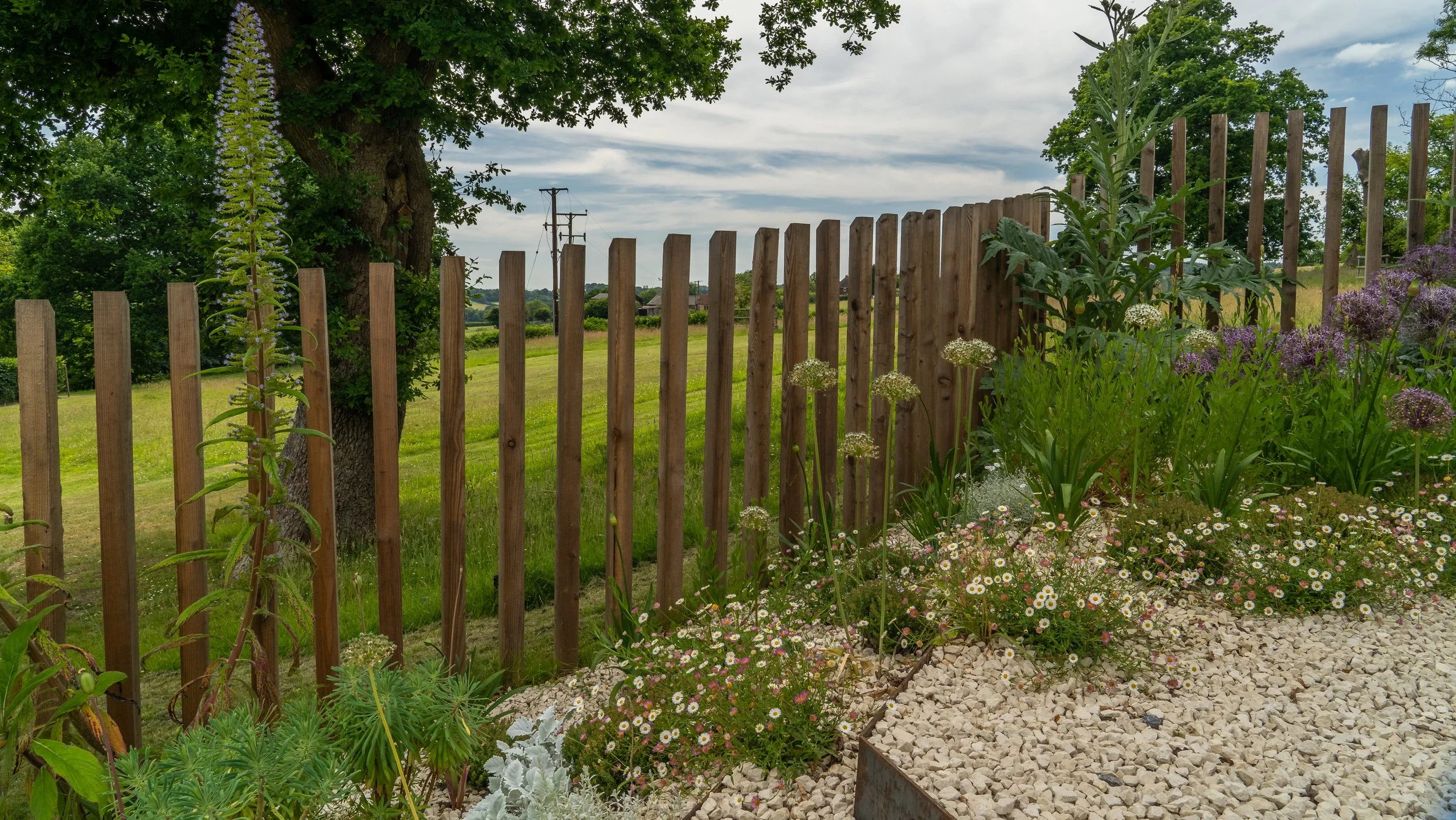 Sculptural timber deer protection rises beside layered planting, with views into the wider landscape at The Paddocks.
