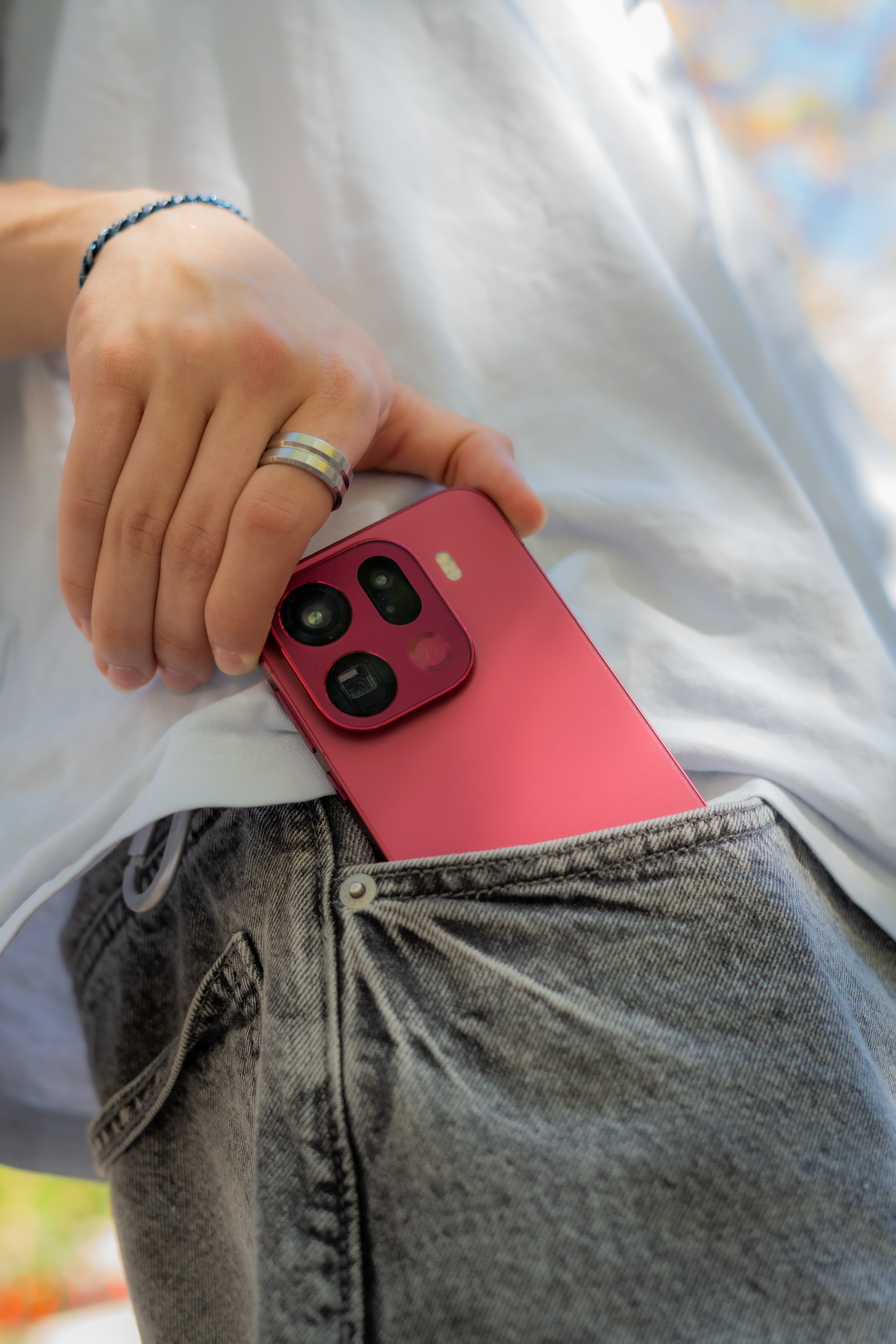 Close-up of a person in gray jeans holding a pink smartphone in their pocket, with a blurred background.