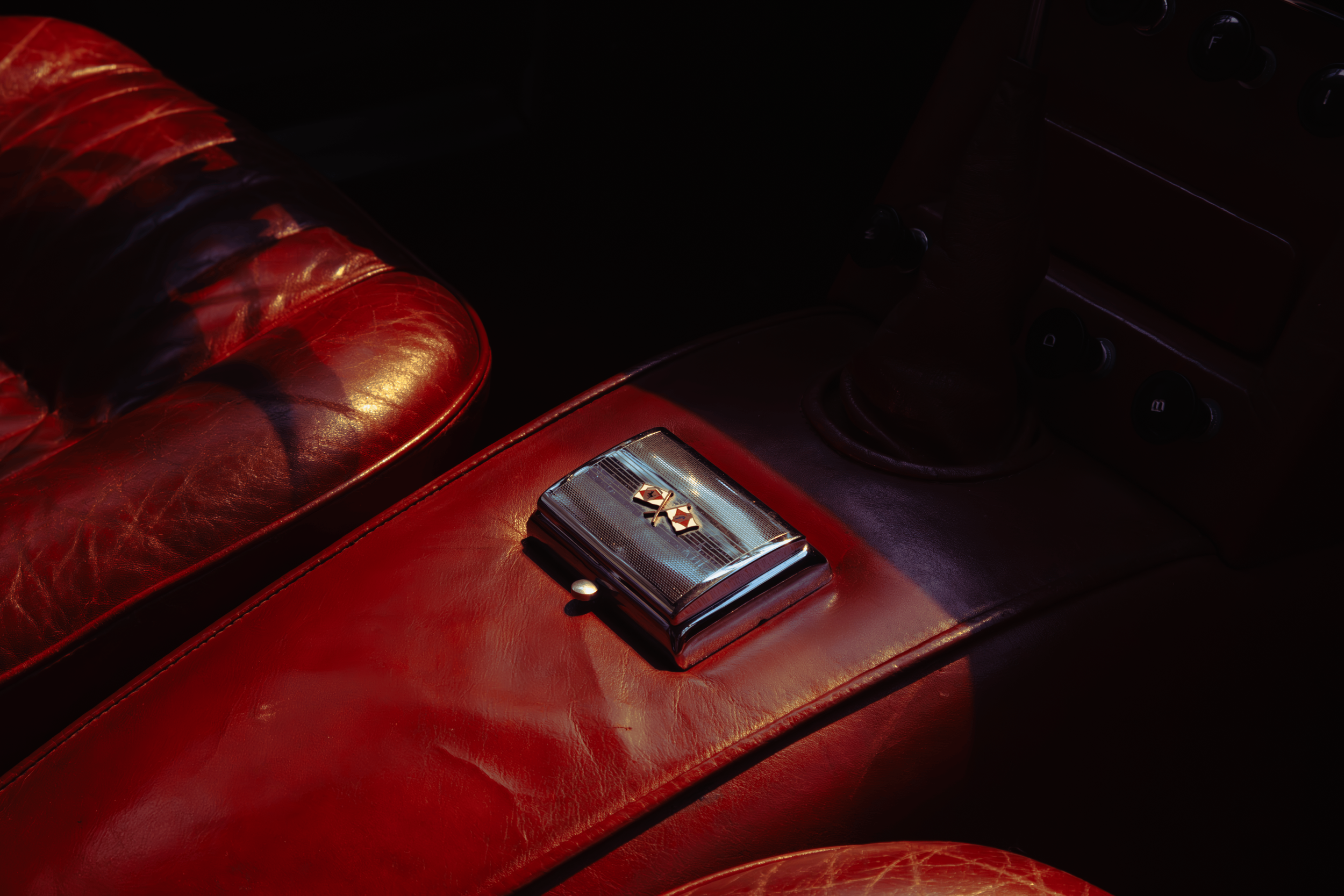 Close-up of a vintage car interior with a red leather seat and a control panel with a badge