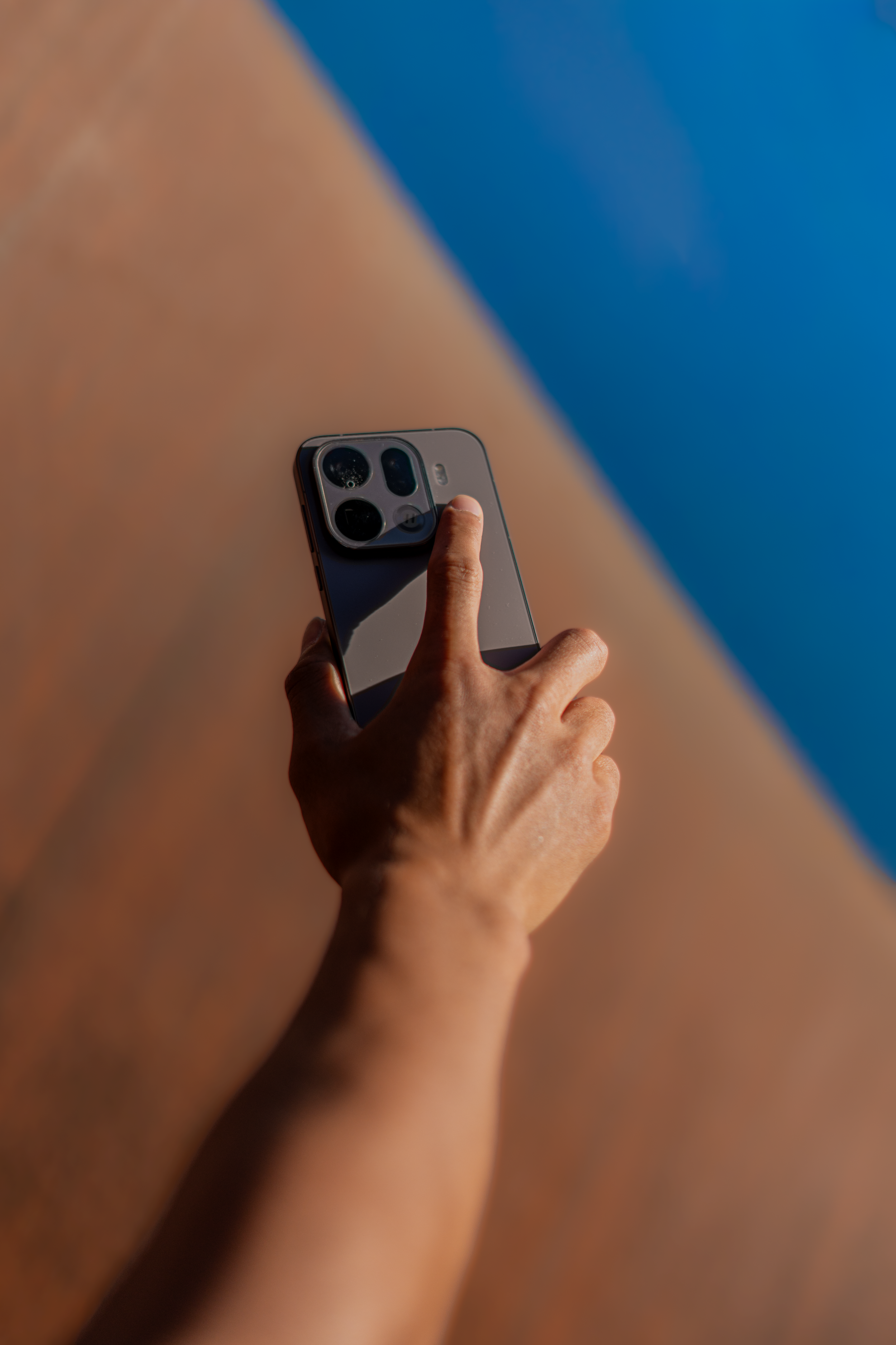 Close-up of a hand holding a smartphone, focusing on the camera lenses, against a background of blurred skin and a blue backdrop.