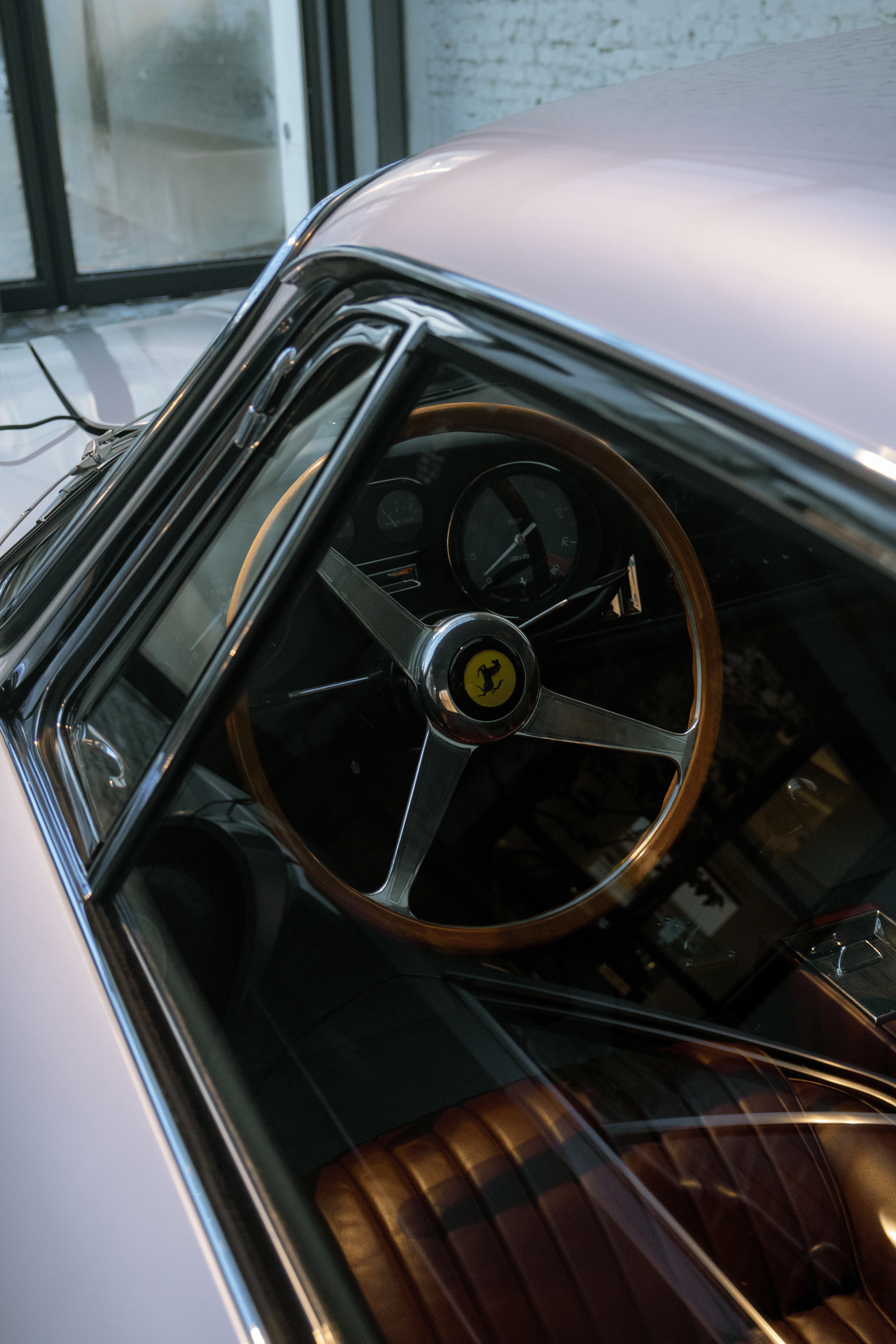 Close-up of the interior of a vintage white Ferrari car, showing the steering wheel with the Ferrari logo, the dashboard with gauges, and part of the leather seats through the car window.