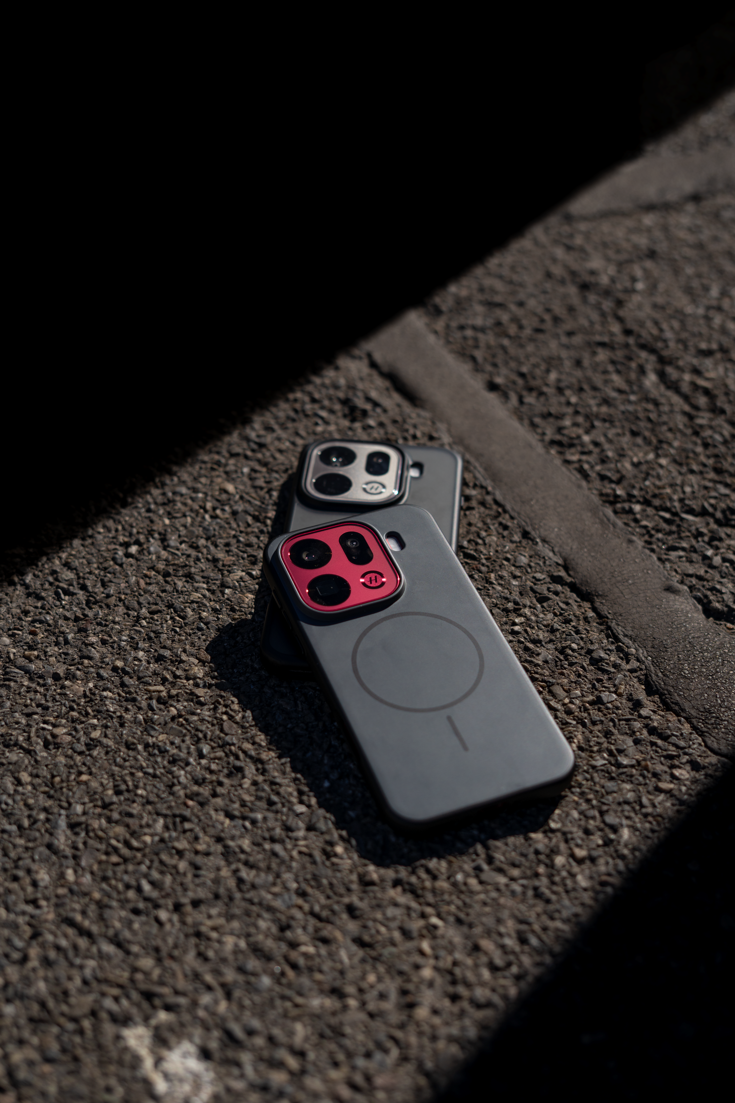 Two iPhones lying face down on a rough concrete surface, partially covered by a shadow.