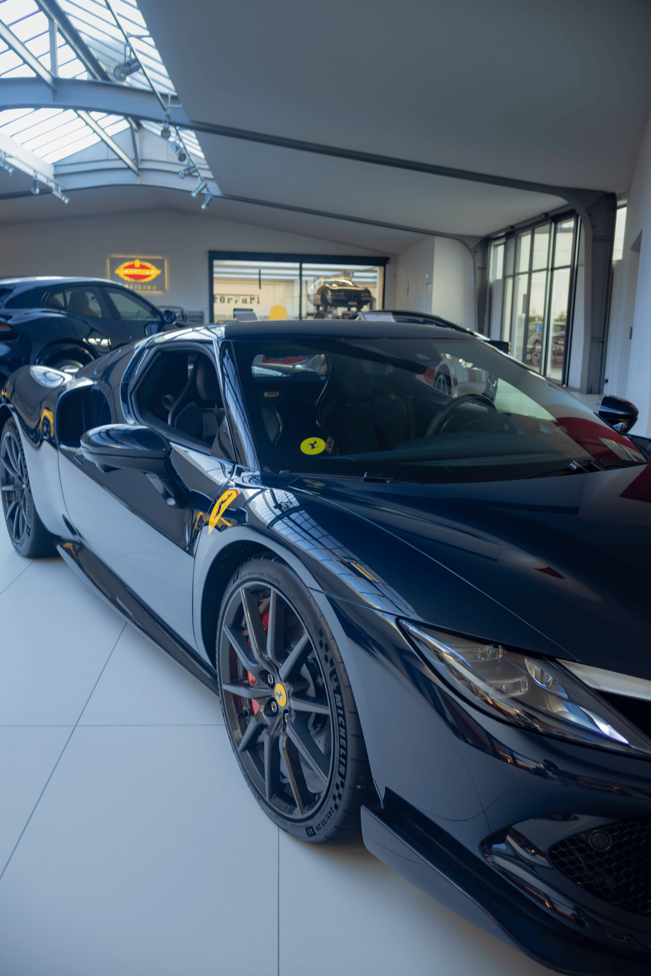 A black Ferrari sports car displayed inside a modern showroom with large windows and white floors